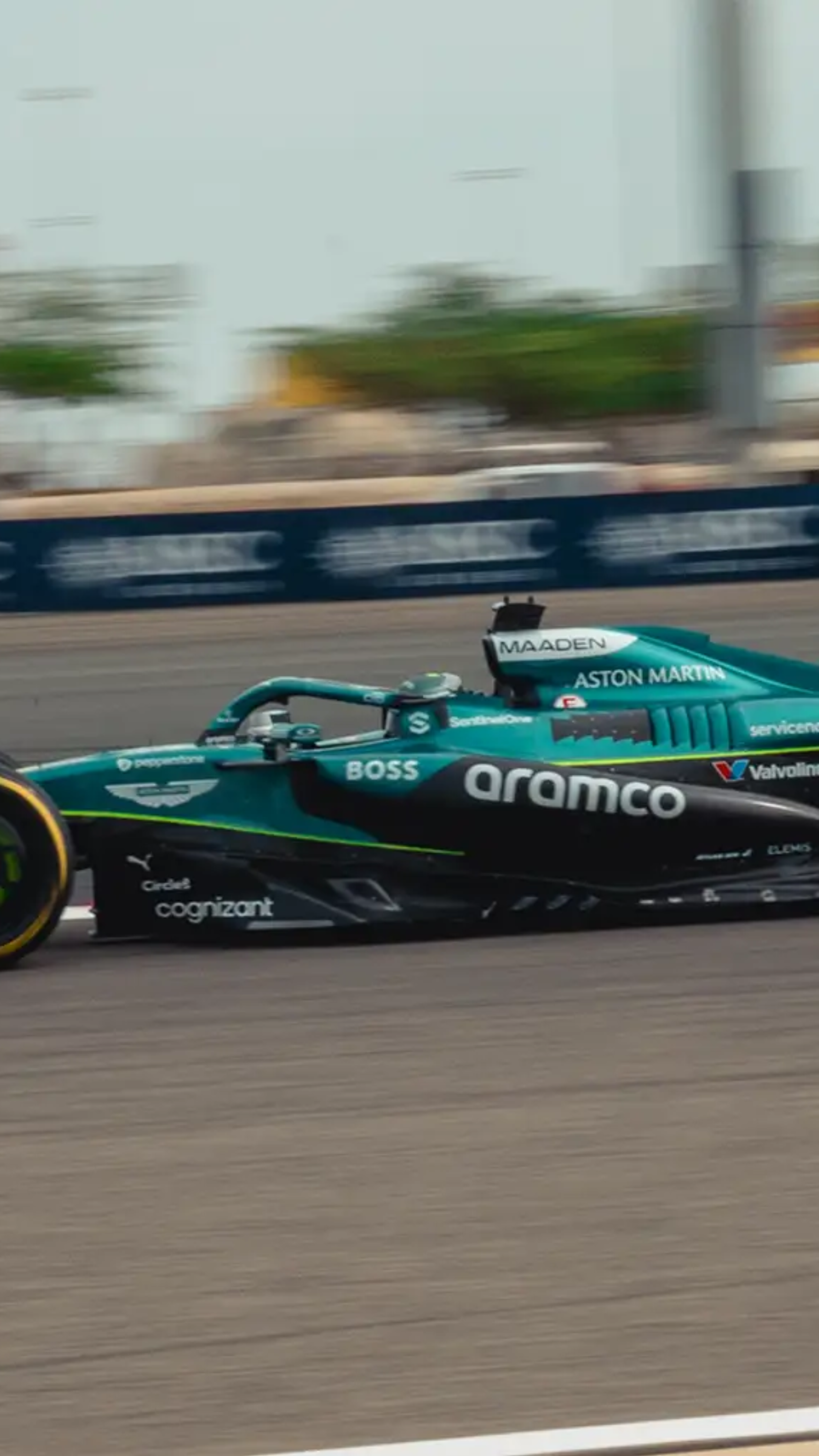 A teal and black Aston Martin F1 car with the number 18 speeds along a racetrack.