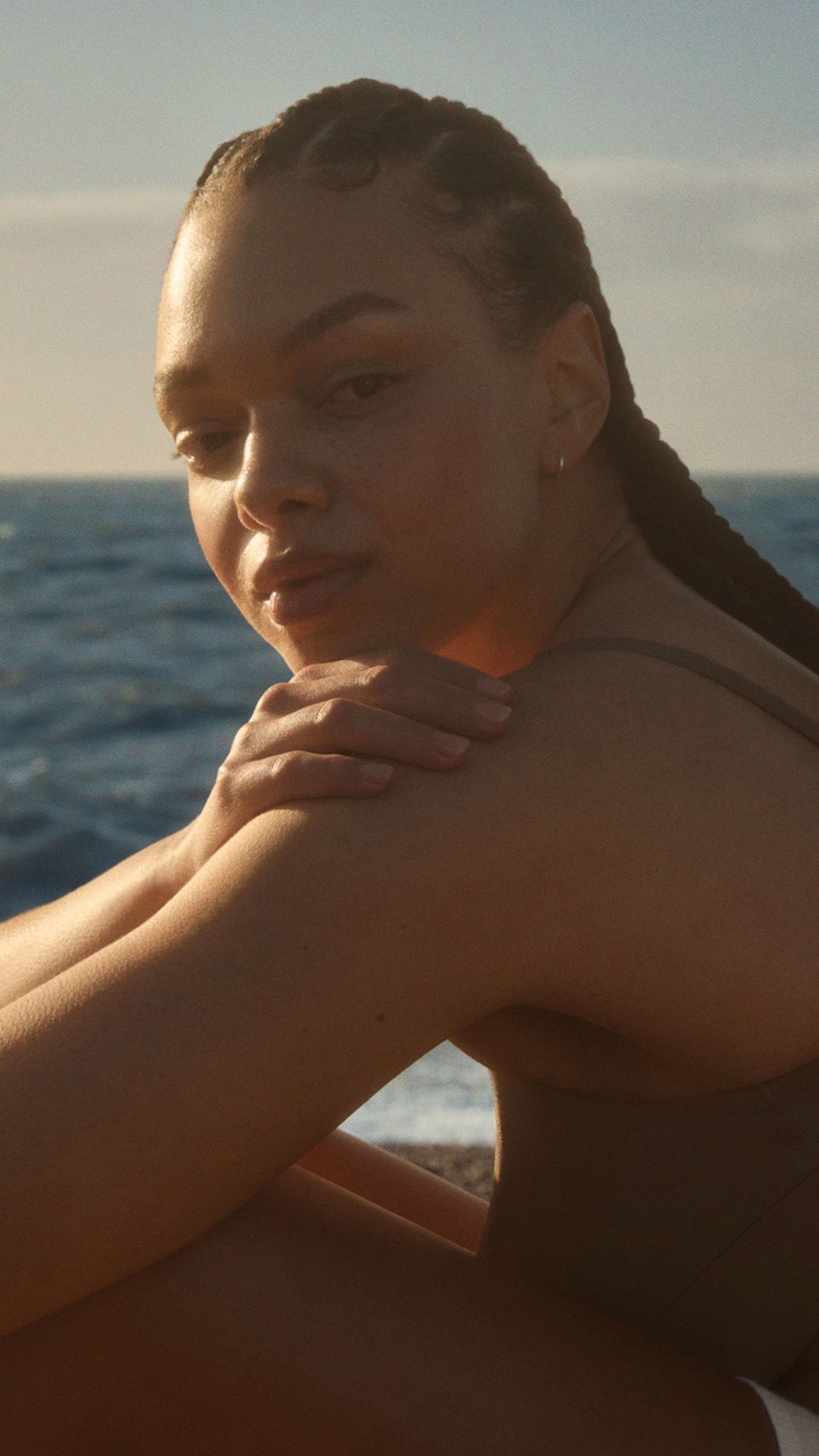Smiling woman with freckles lying in grass, shielding her face from the sun.