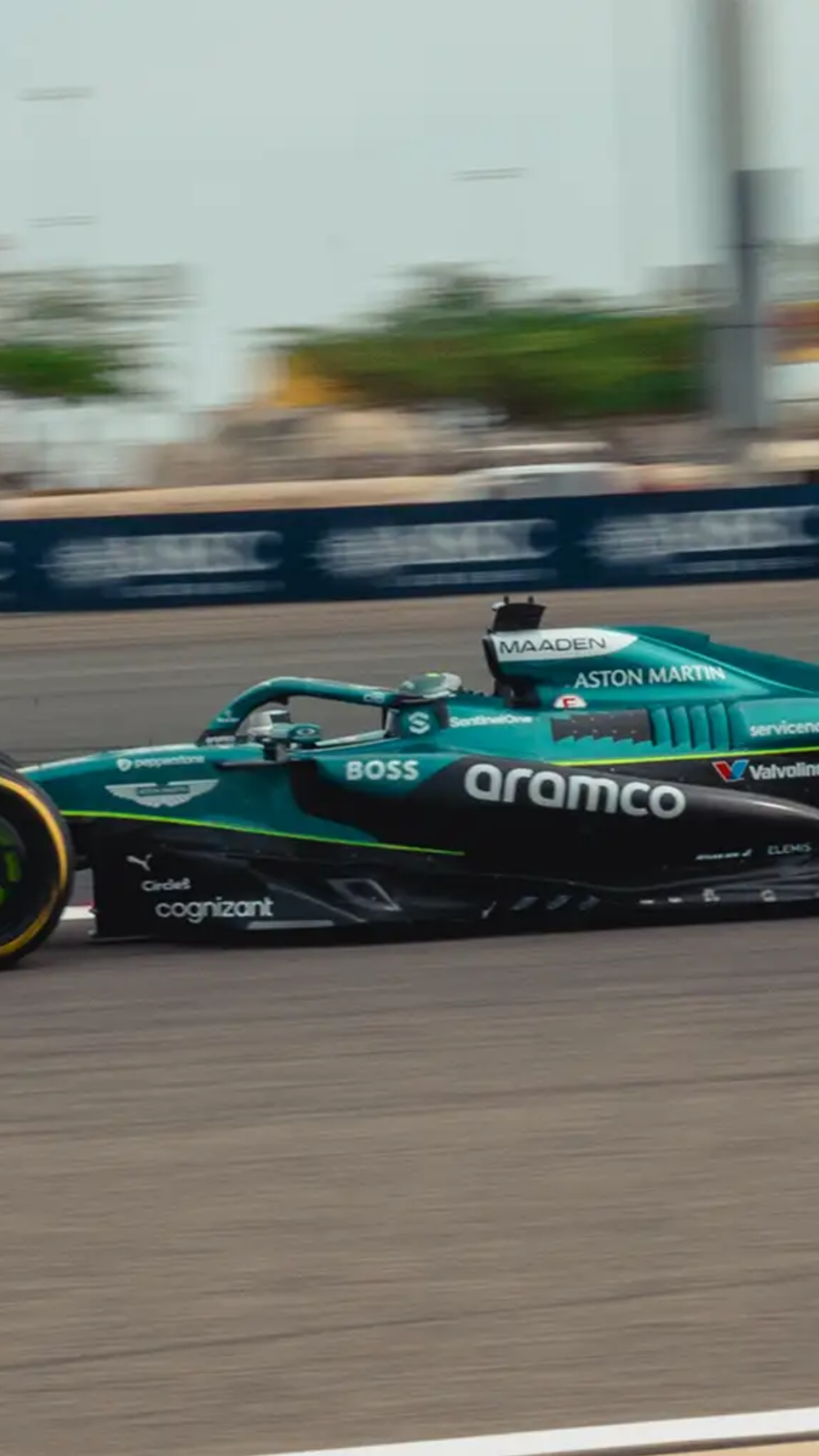 A teal and black Aston Martin F1 car with the number 18 speeds along a racetrack.