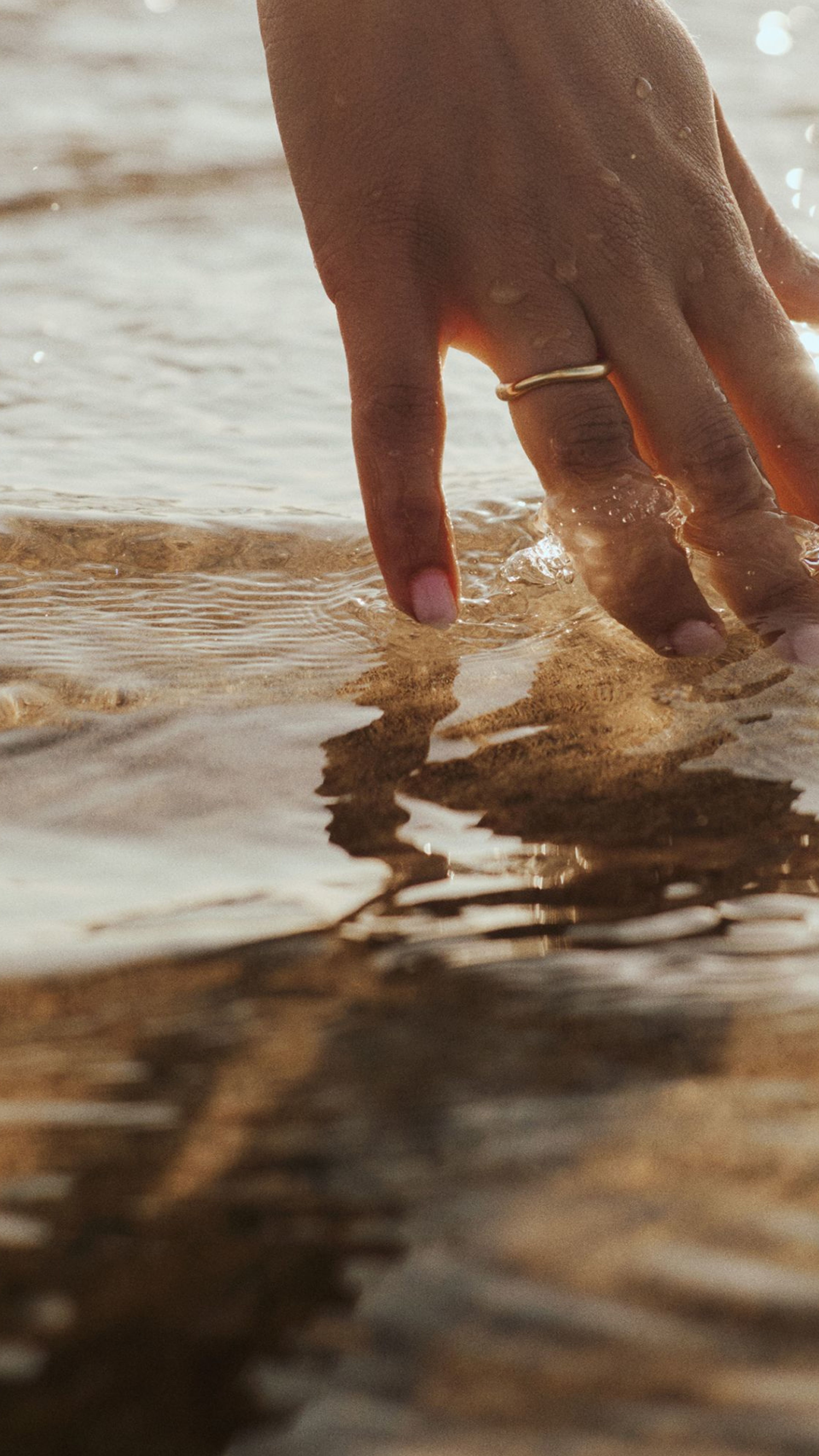 A hand with a gold ring gently touches sparkling water.