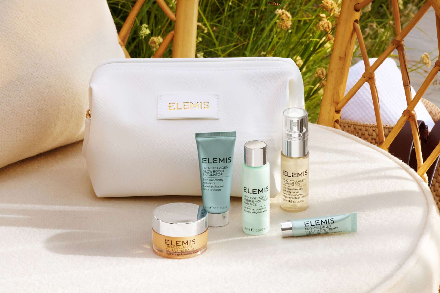 A navy Elemis cosmetic bag and Pro-Collagen skincare products sit on a stone surface next to a swimming pool.