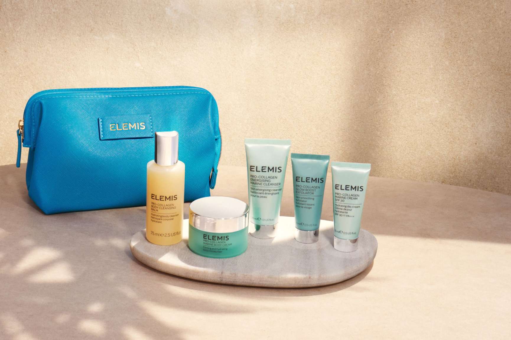 A navy Elemis cosmetic bag and Pro-Collagen skincare products sit on a stone surface next to a swimming pool.