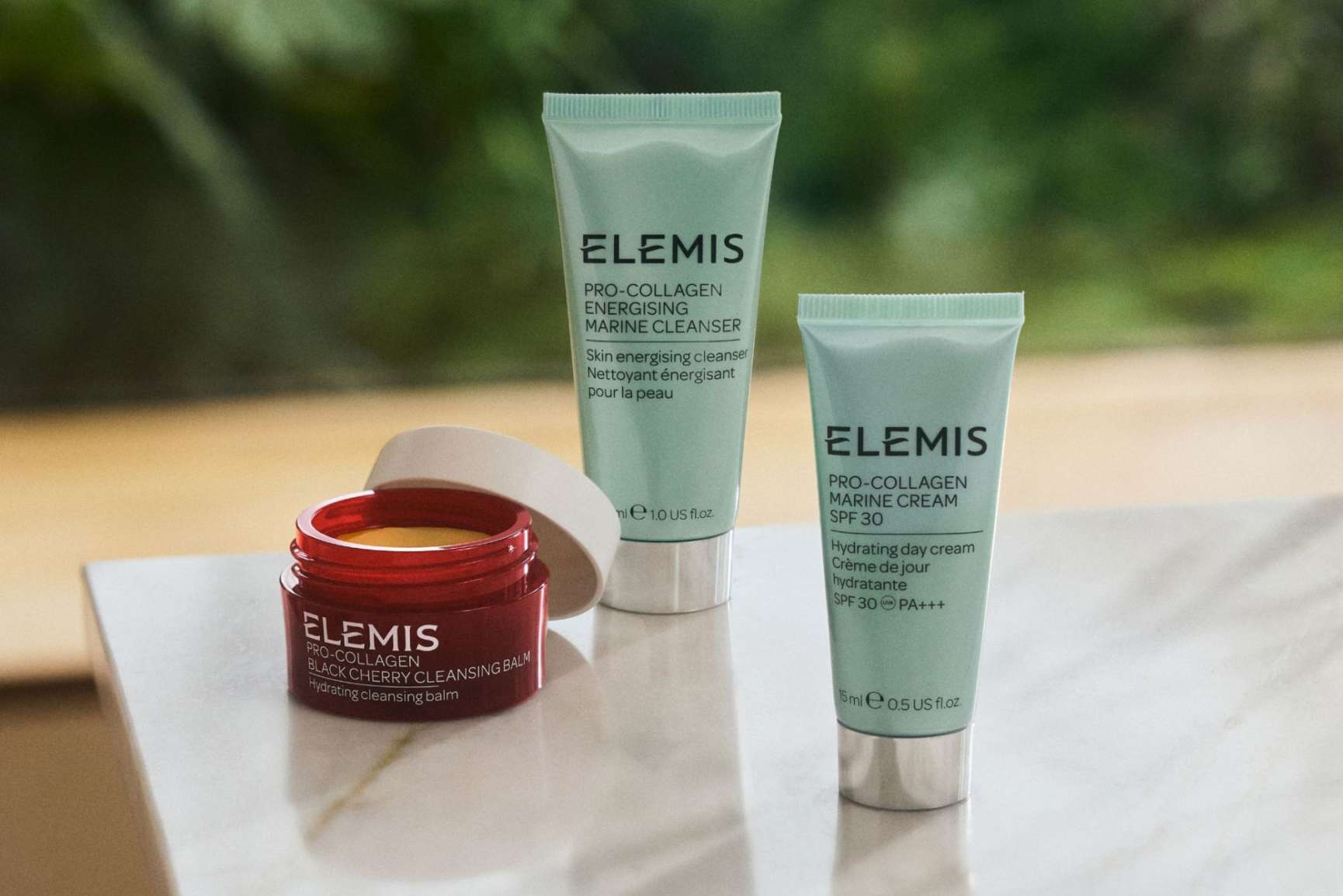 Three Elemis Pro-Collagen products: an open red jar of cleansing balm, and two mint green tubes of cleanser and marine cream.