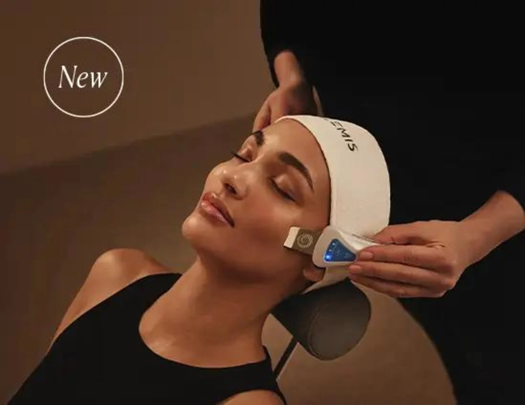 A woman receives a facial massage, with several skincare capsules on the white bedsheet.