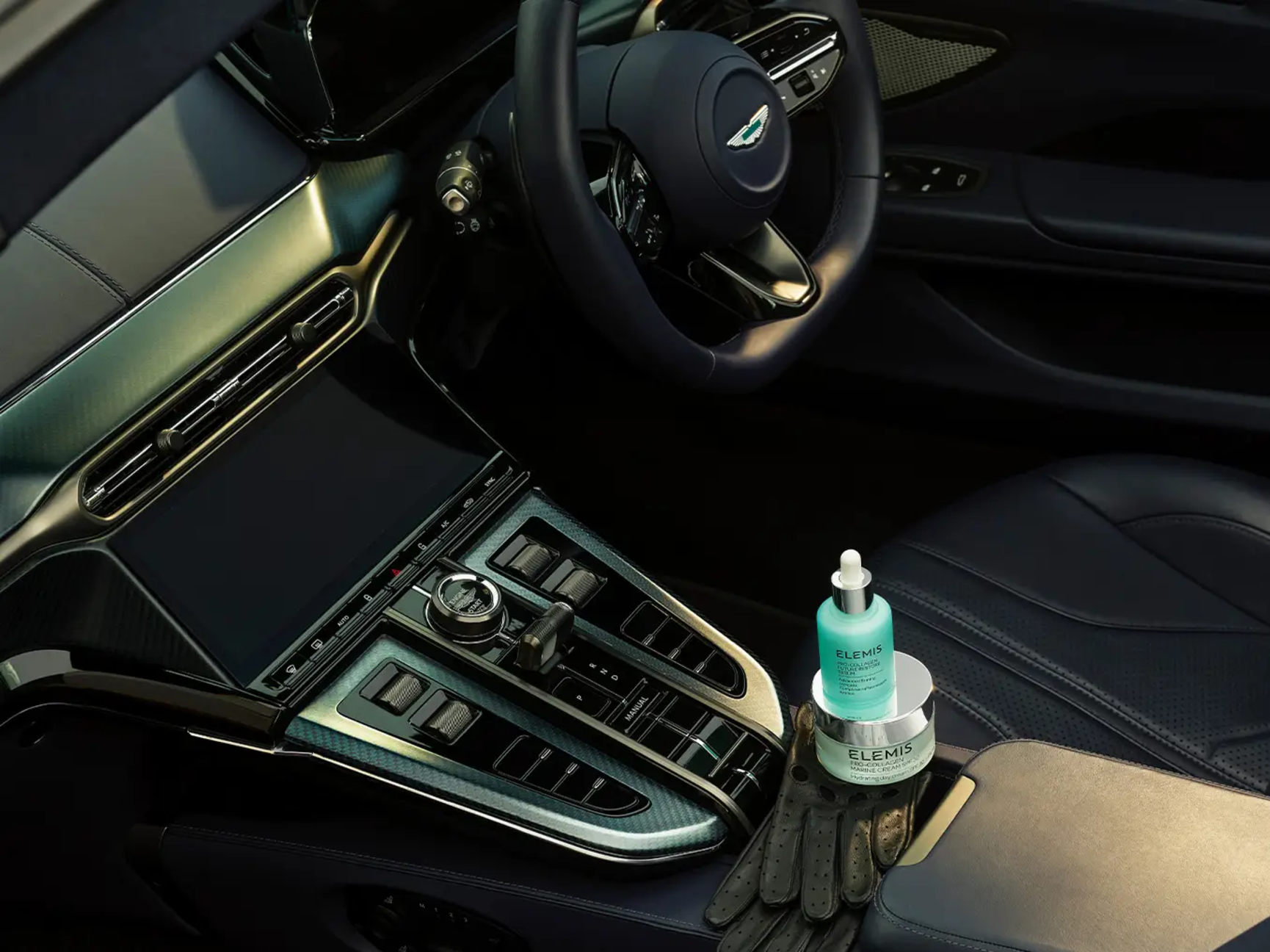 Elemis skincare products and black leather gloves in an Aston Martin car interior.
