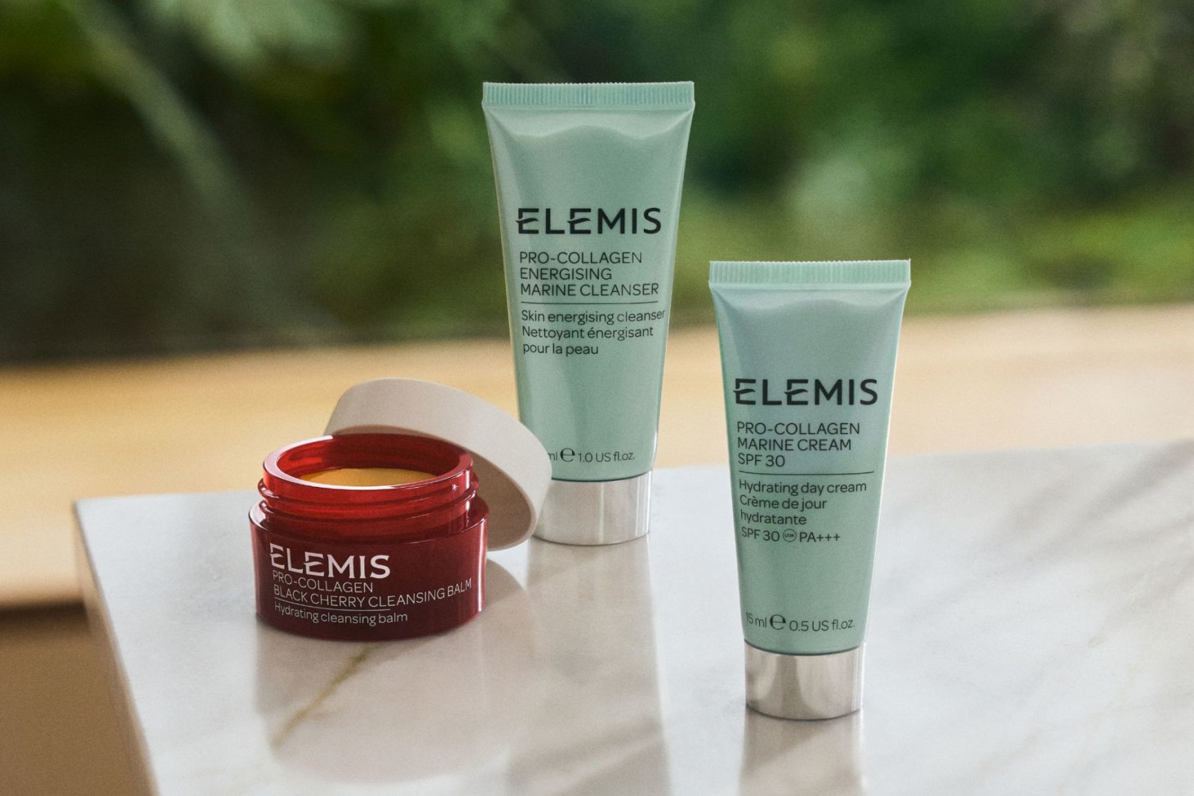 Three Elemis Pro-Collagen products: an open red jar of cleansing balm, and two mint green tubes of cleanser and marine cream.