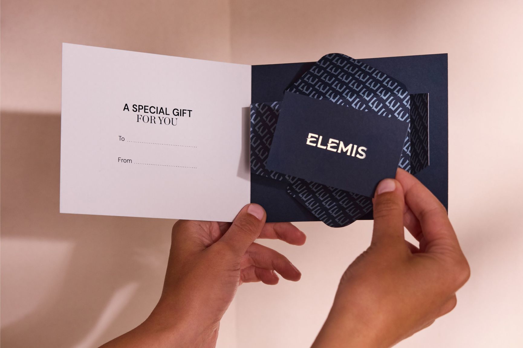 Un tarjetero de regalo ELEMIS abierto en color azul marino que muestra una tarjeta de regalo con un logotipo dorado y el mensaje «UN REGALO ESPECIAL PARA USTED».