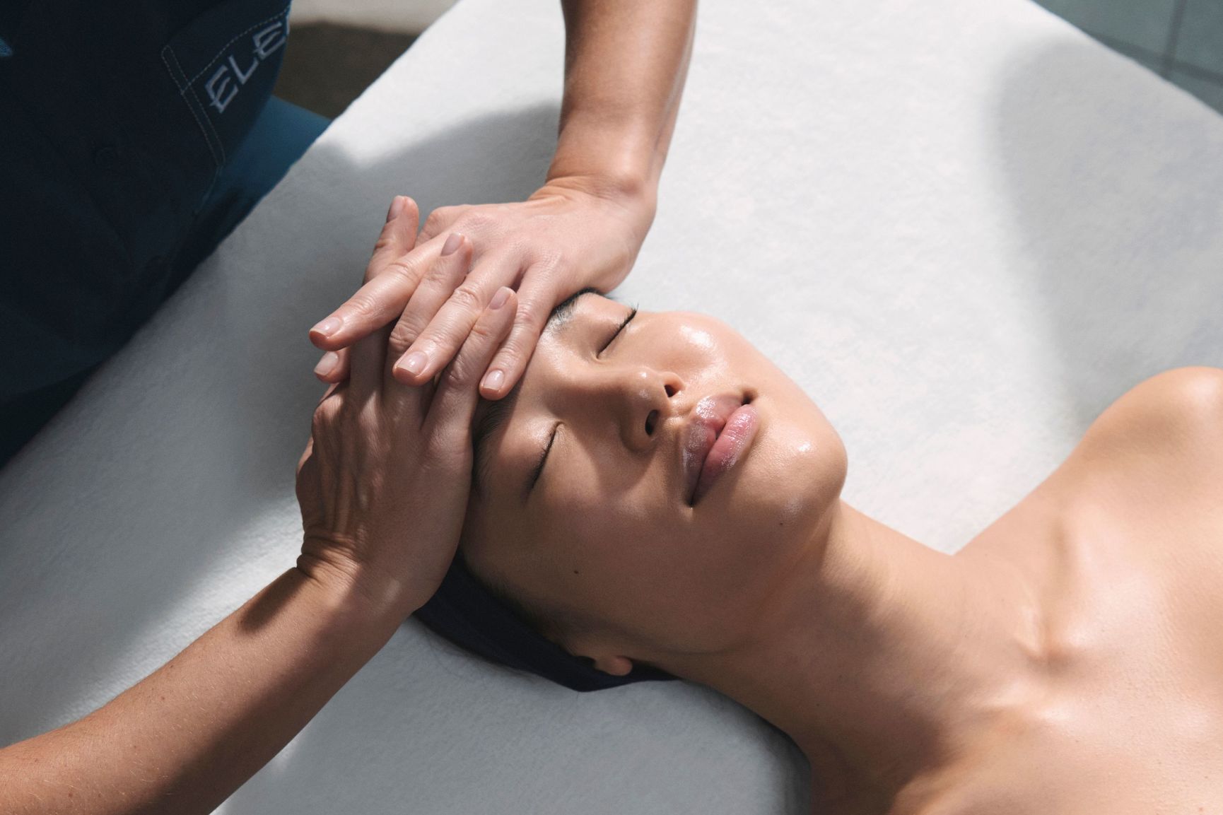 A woman receives an Elemis facial with cooling globes applied to her cheeks by a therapist.