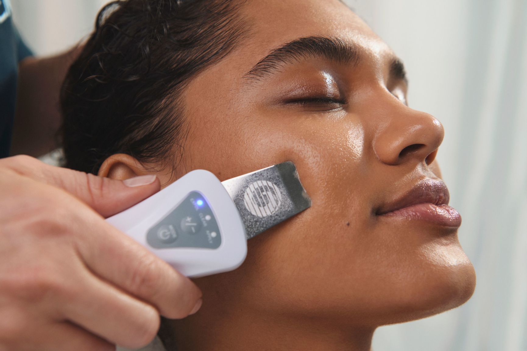 A woman receives a facial massage, with several skincare capsules on the white bedsheet.