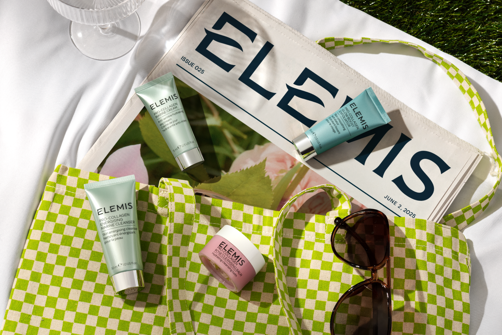 Checkered green and tan tote bag with products laying on top as well as sunglasses and an ELEMIS newspaper.