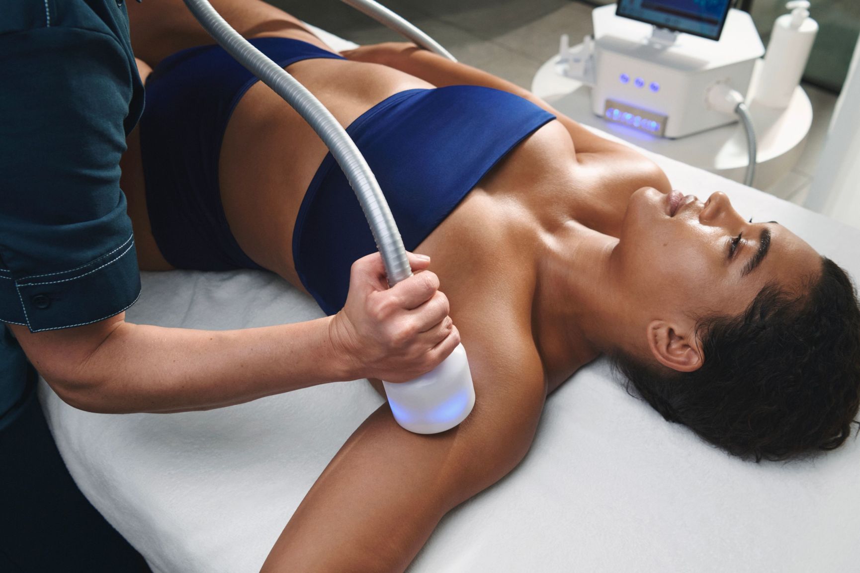 A technician uses a handheld device to treat a woman's upper arm.