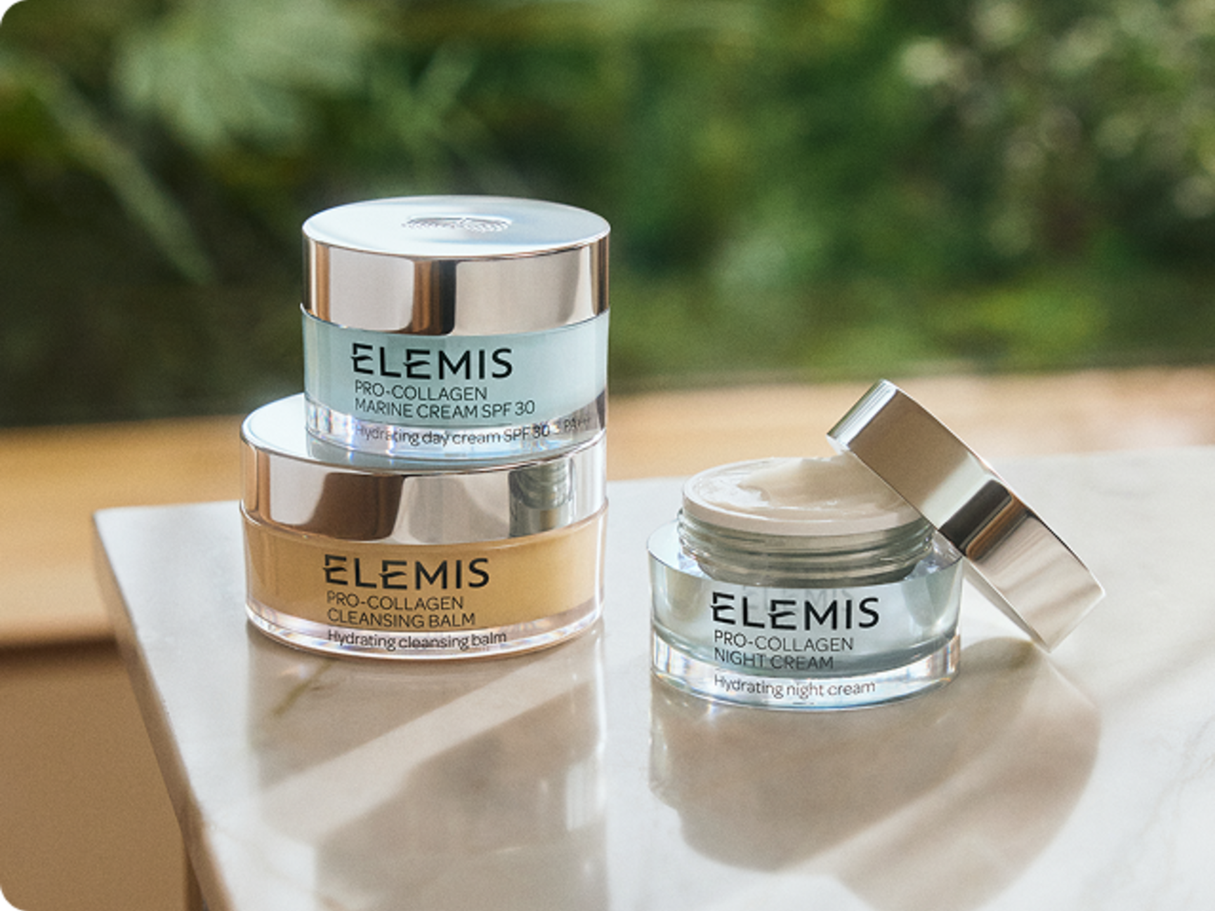 Elemis Pro-Collagen Cleansing Balm, Toning Mist, and Marine Cream on a bathroom counter.