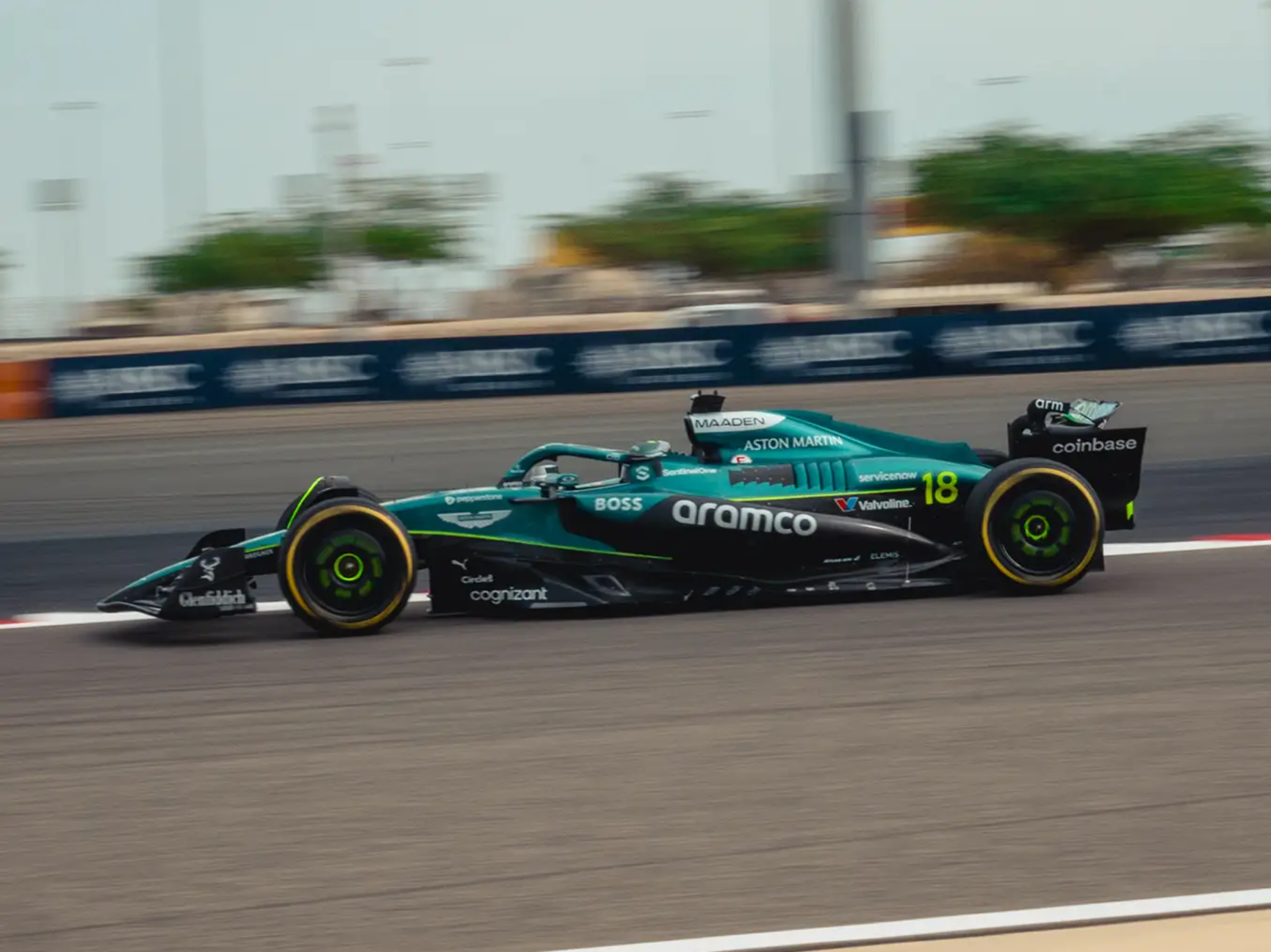 A teal and black Aston Martin F1 car with the number 18 speeds along a racetrack.