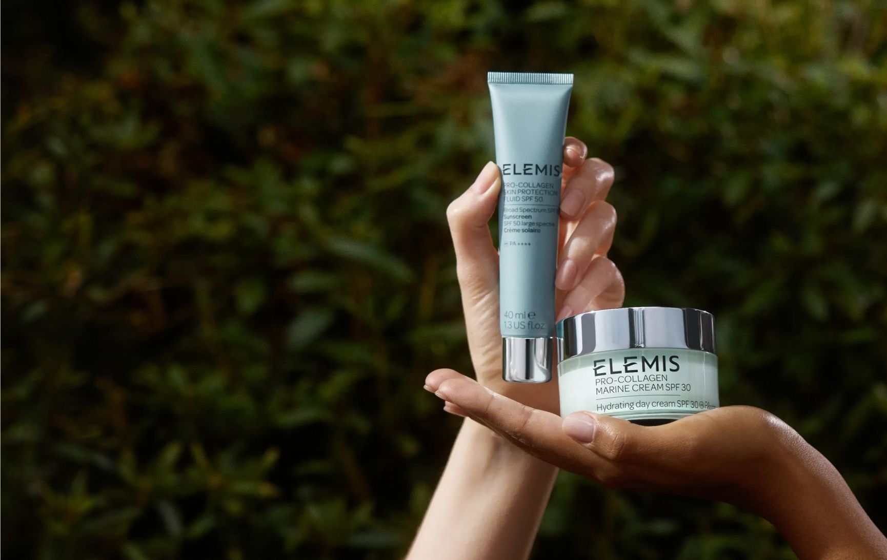 Hands holding an Elemis Pro-Collagen Marine Cream SPF 30 tube and jar against a green background.
