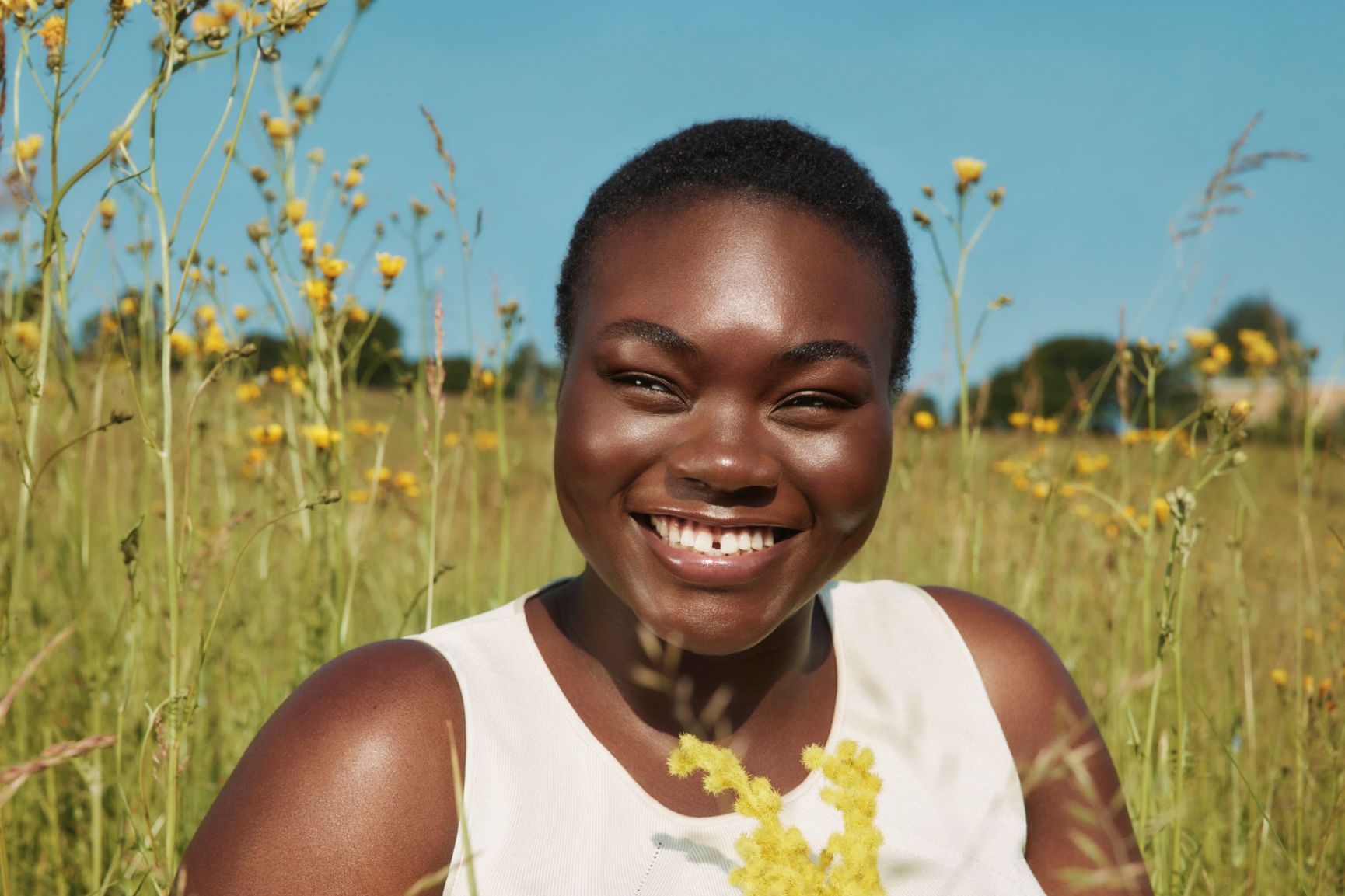Smiling Black woman in a sunny field of yellow wildflowers.