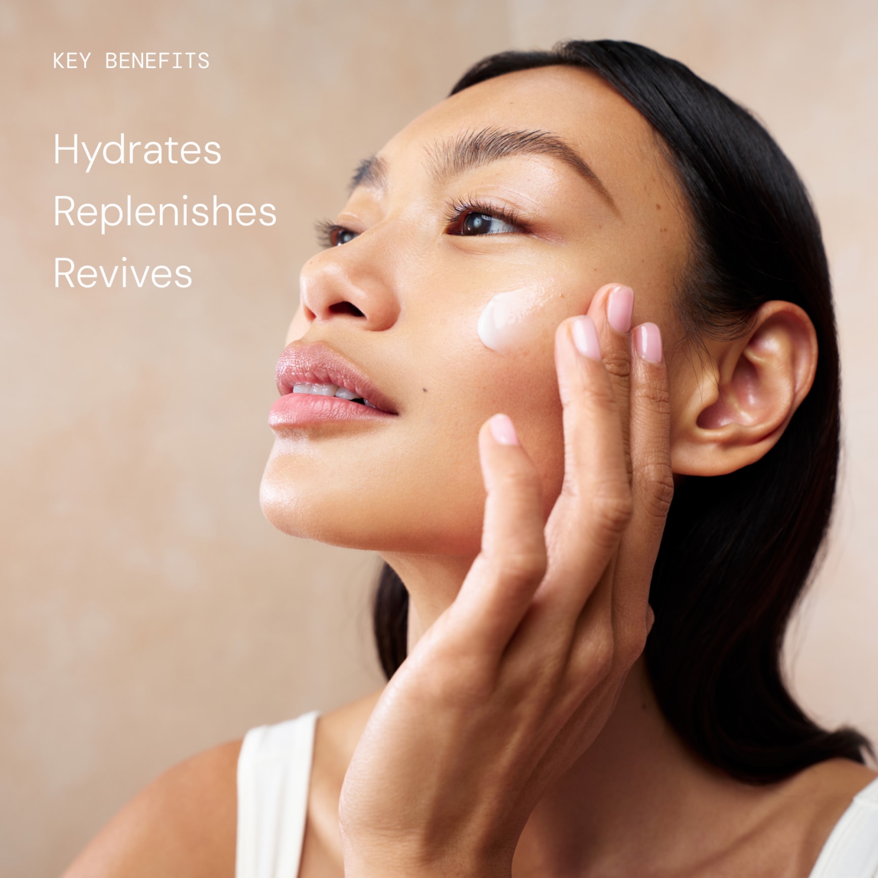 Woman applying face cream to her cheek on beige background with text: “Key benefits: Hydrates, Replenishes, Revives”.