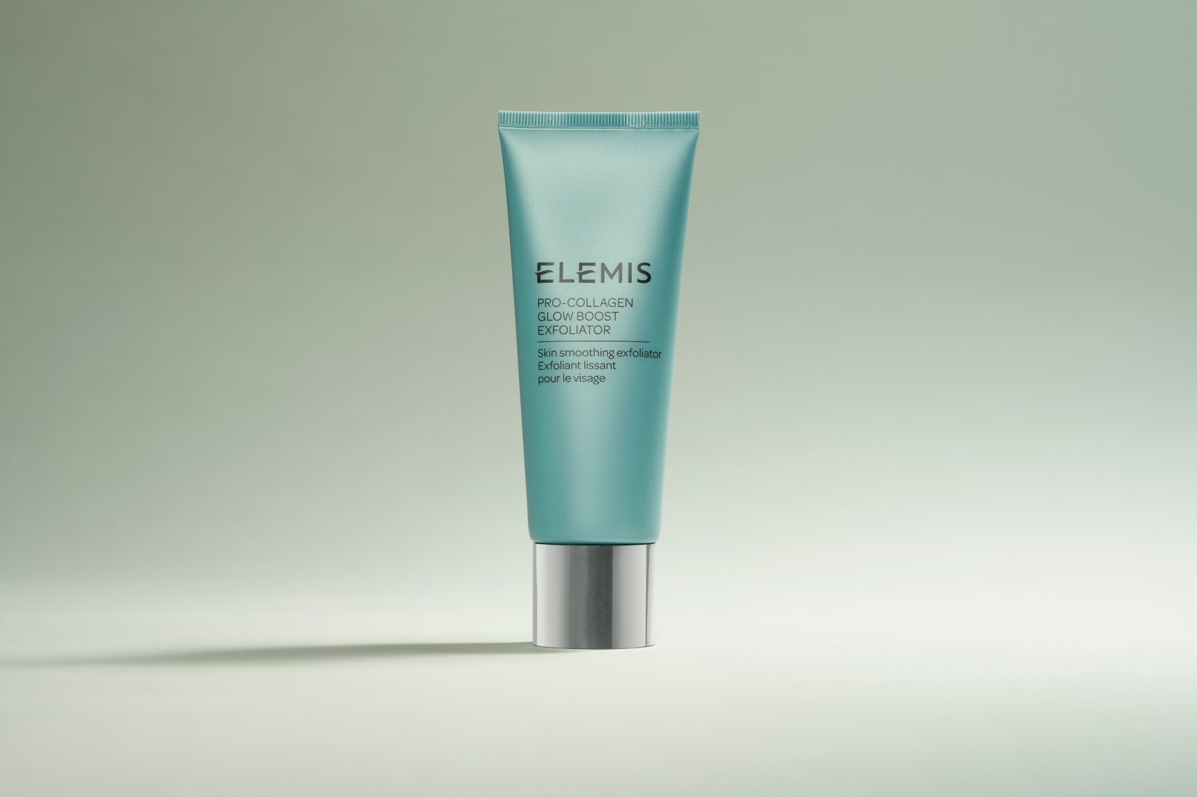 Multiple teal Elemis Pro-Collagen Glow Boost Exfoliator tubes with silver caps scattered on a light background.