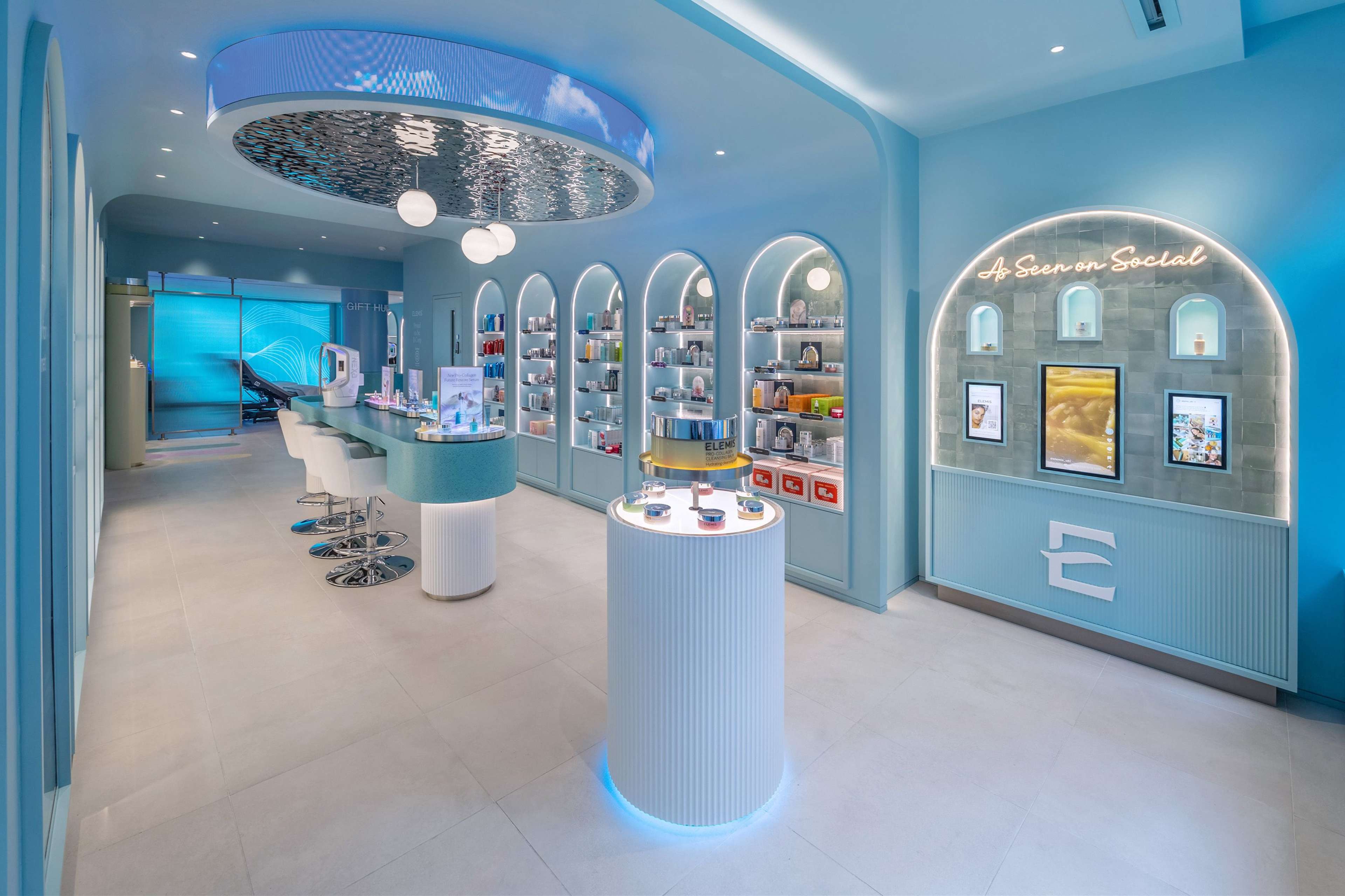 A modern, aqua-blue beauty store with arched product displays, a counter, a circular ceiling screen, and a neon "As Seen on Social" sign.