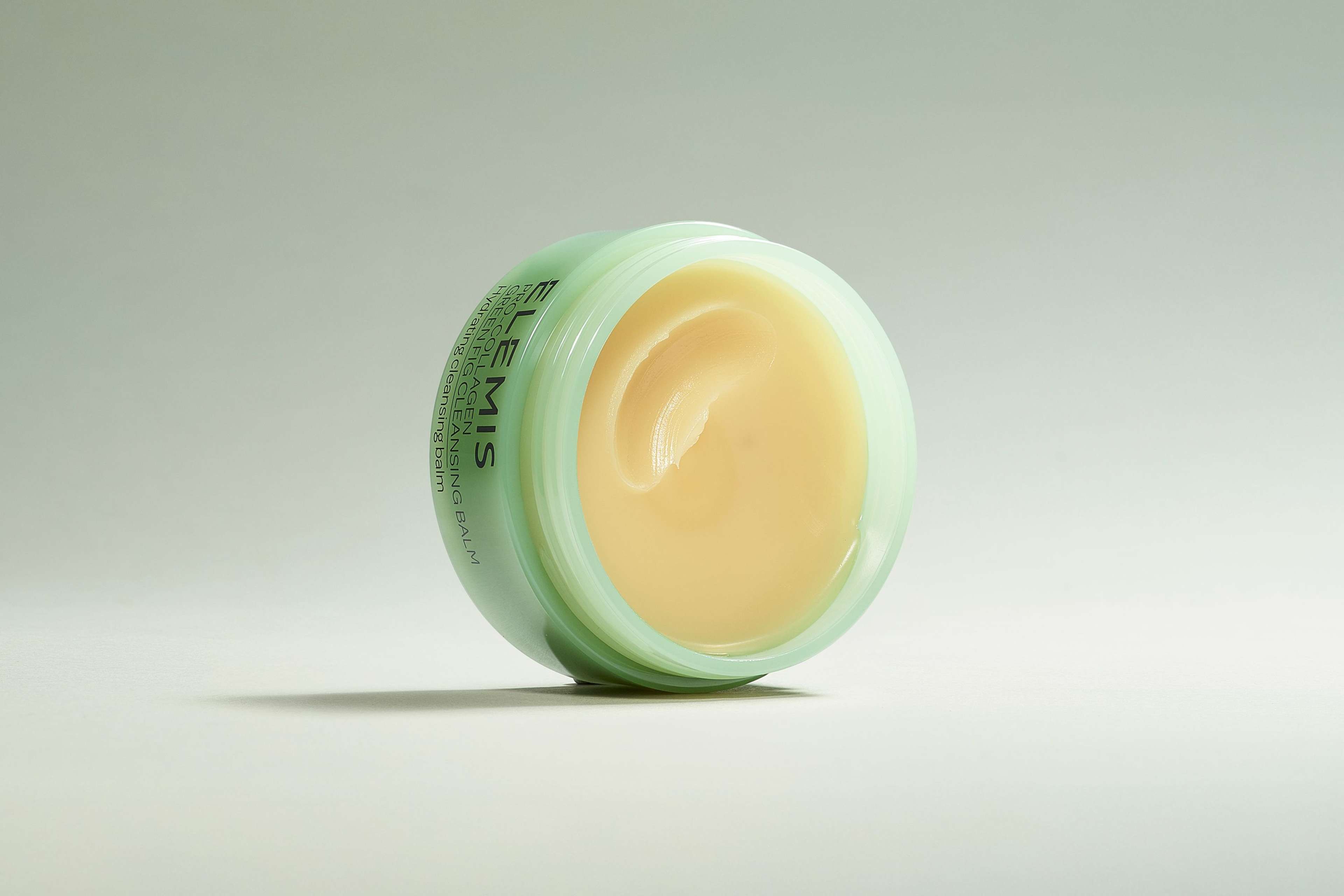 Elemis Pro-Collagen Cleansing Balm in vari colori, uno aperto e quattro impilati, disposti con frutta e fiori.