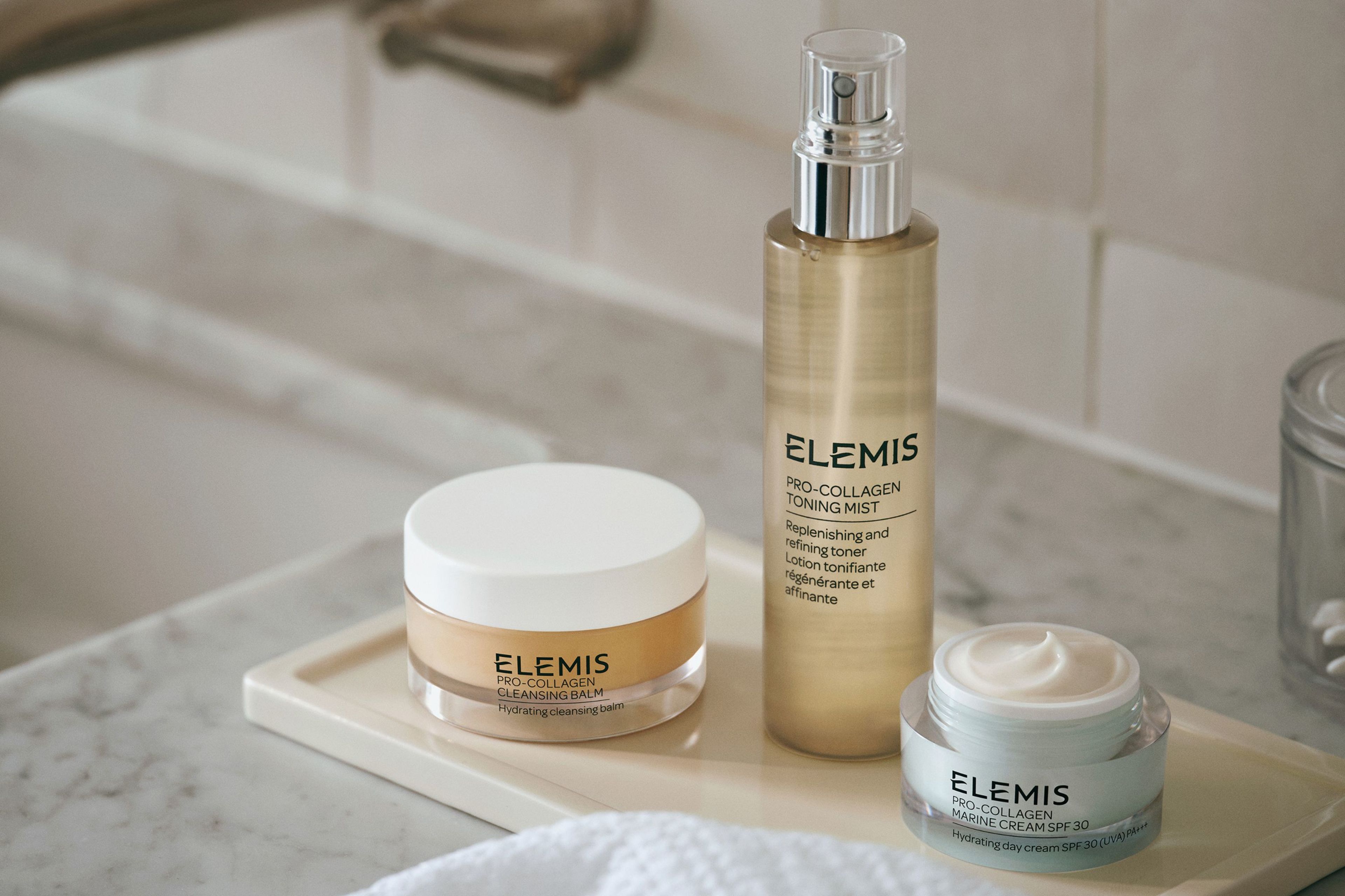 Elemis Pro-Collagen Cleansing Balm, Toning Mist, and Marine Cream on a bathroom counter.