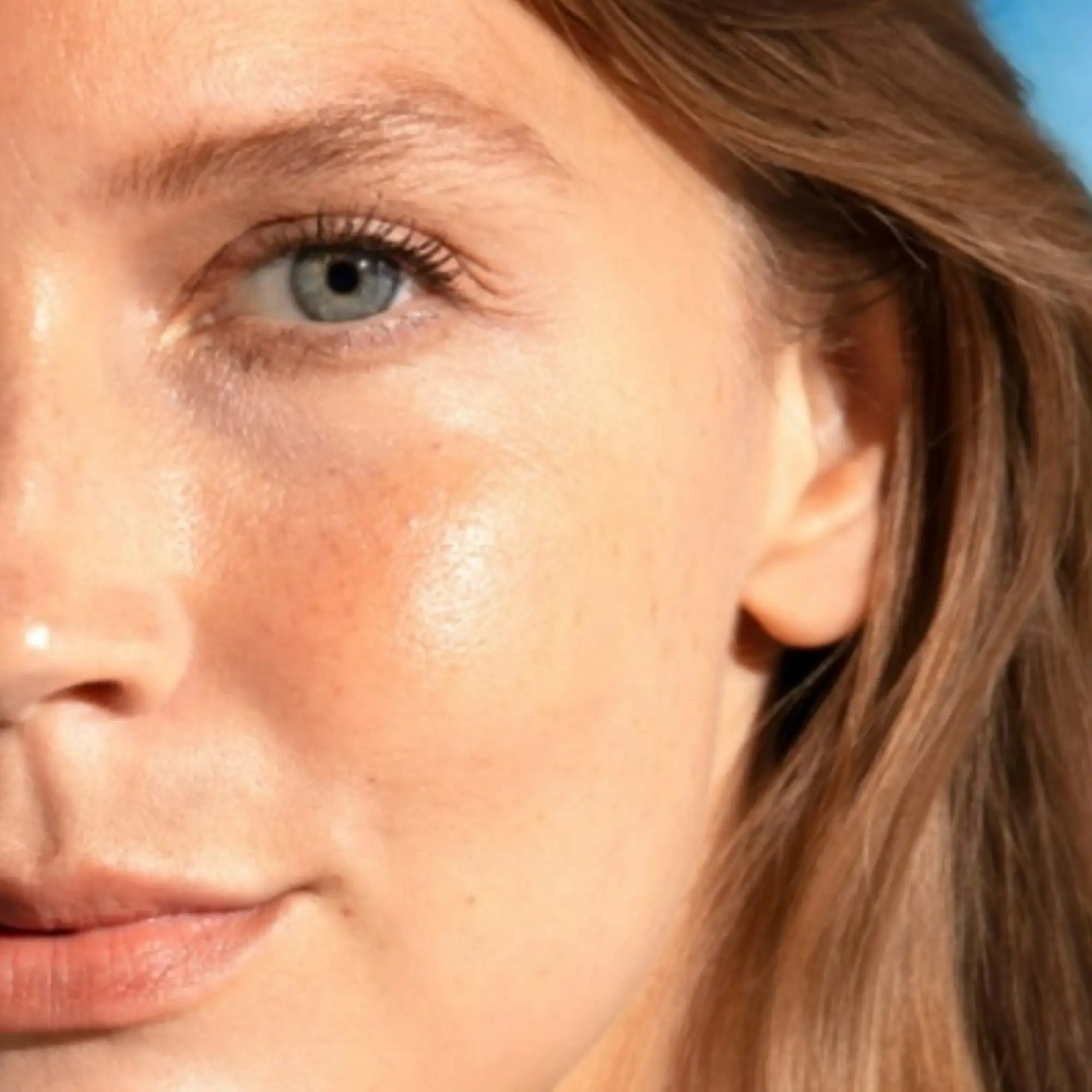 Close-up of a woman's face with a blue eye, visible freckles, and glowing skin.