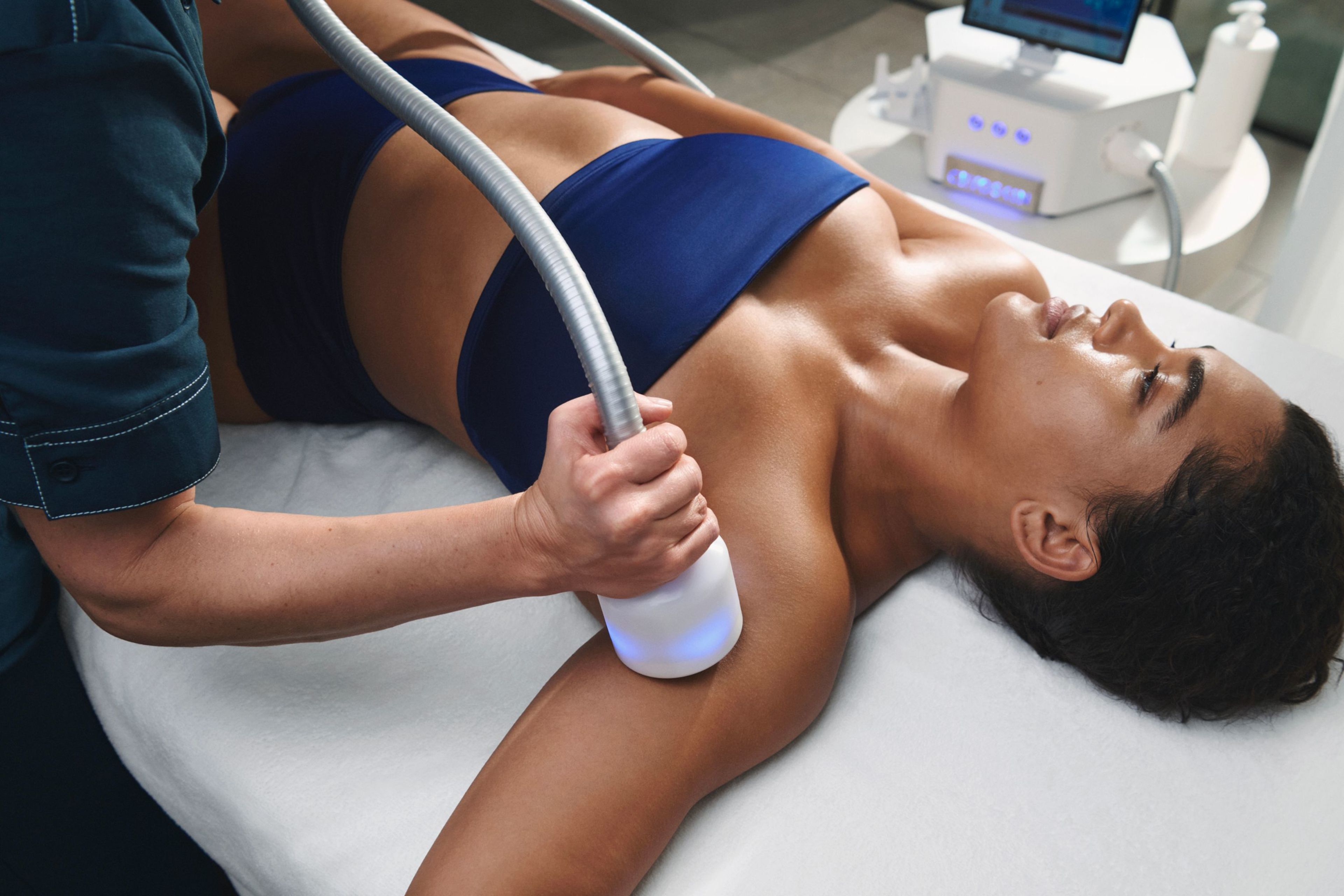 A technician uses a handheld device to treat a woman's upper arm.