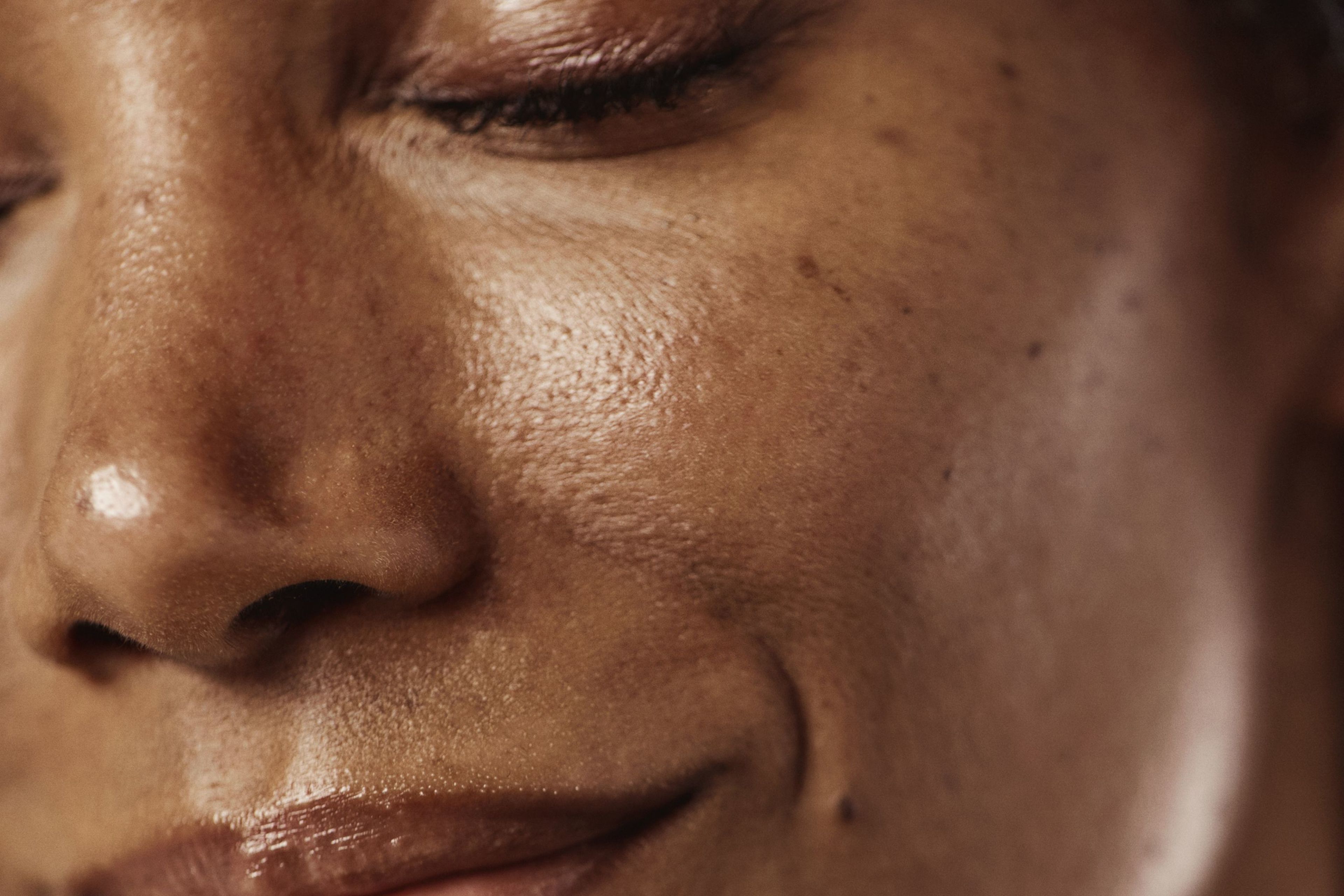 Close-up of a person's face with closed eyes and a gentle smile, showing hydrated brown skin.