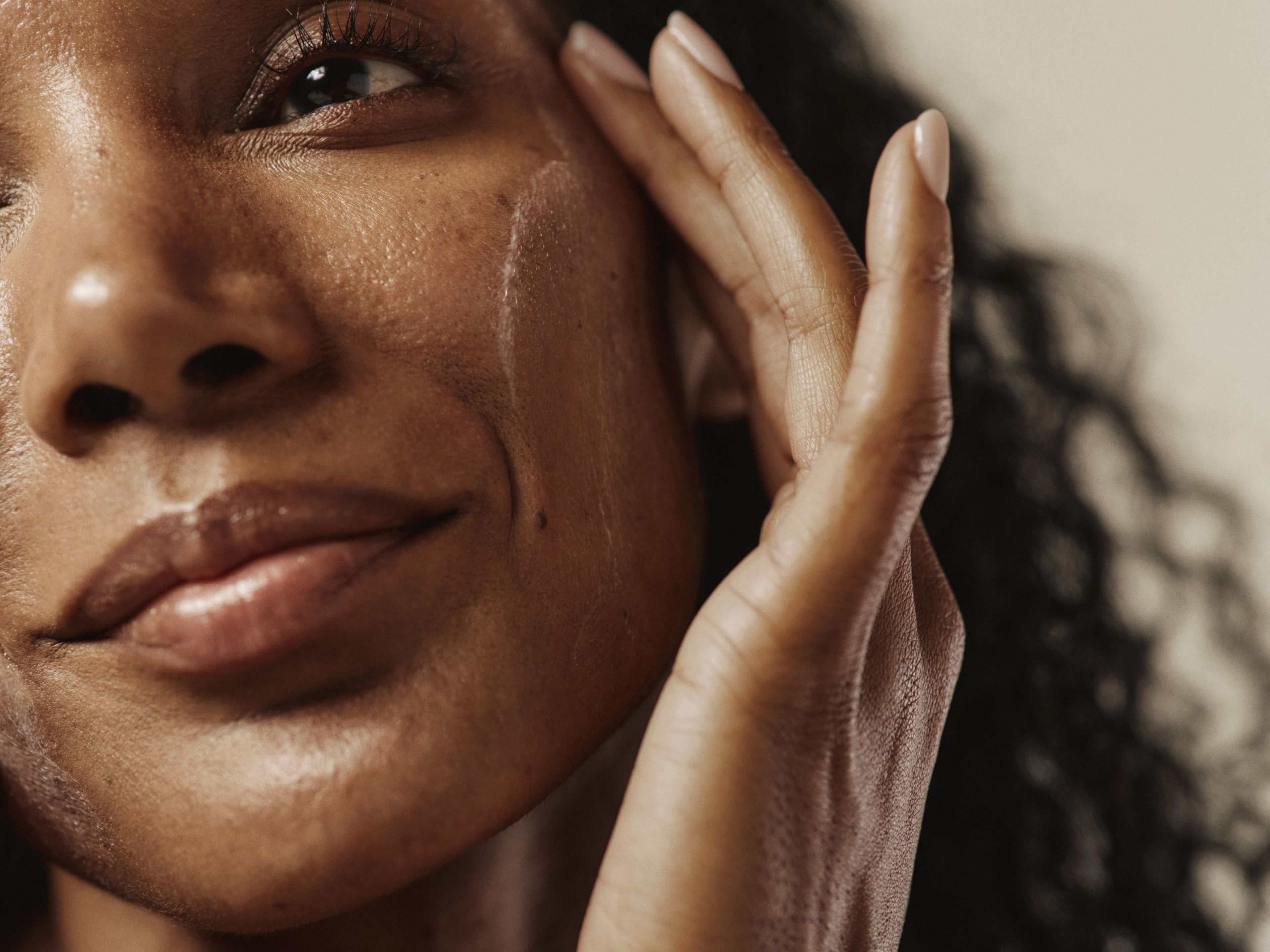 Close-up of a person's face with a hand applying product, leaving streaks on the cheek.