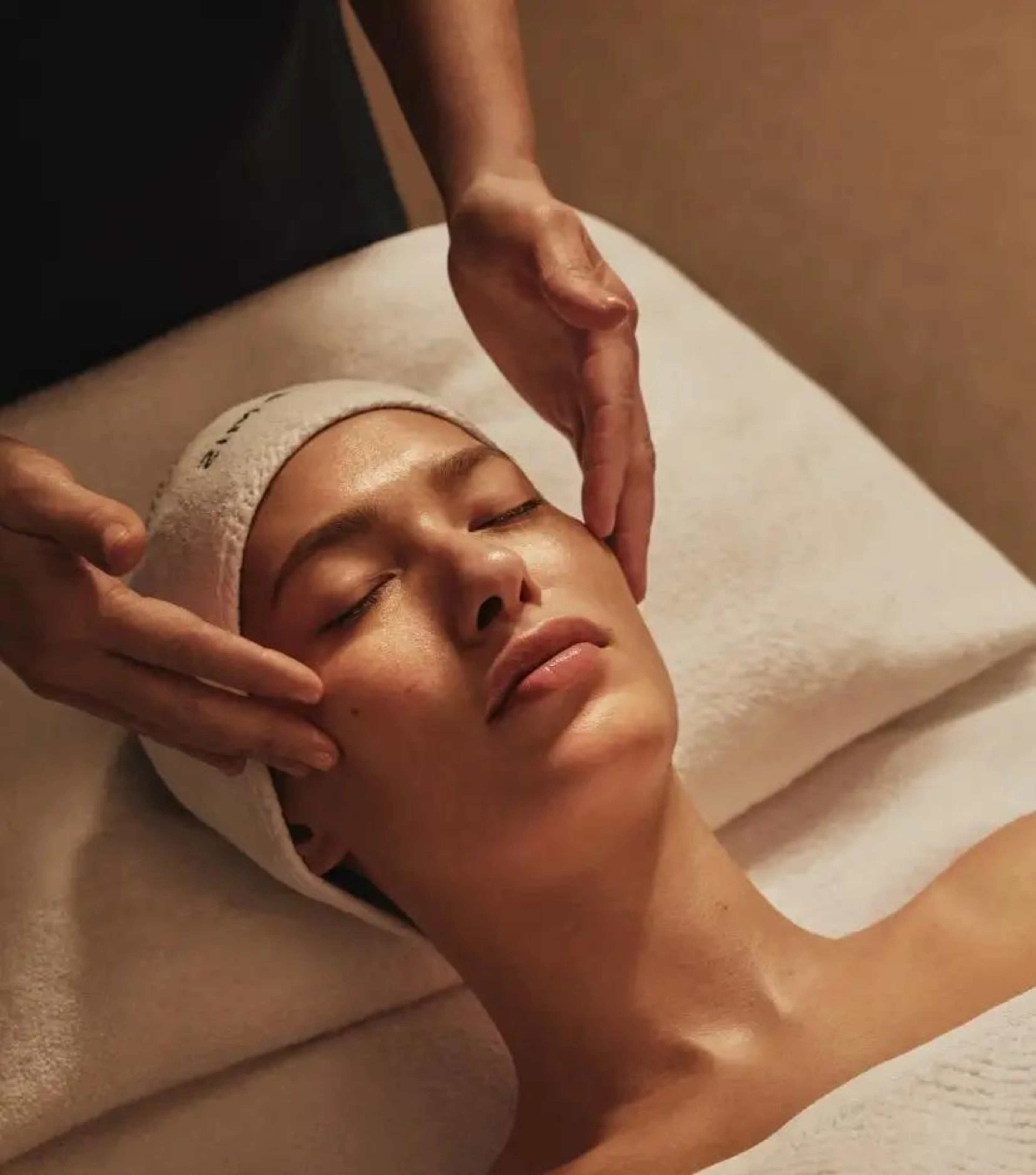 Relaxed woman with a white headband receiving a facial massage.