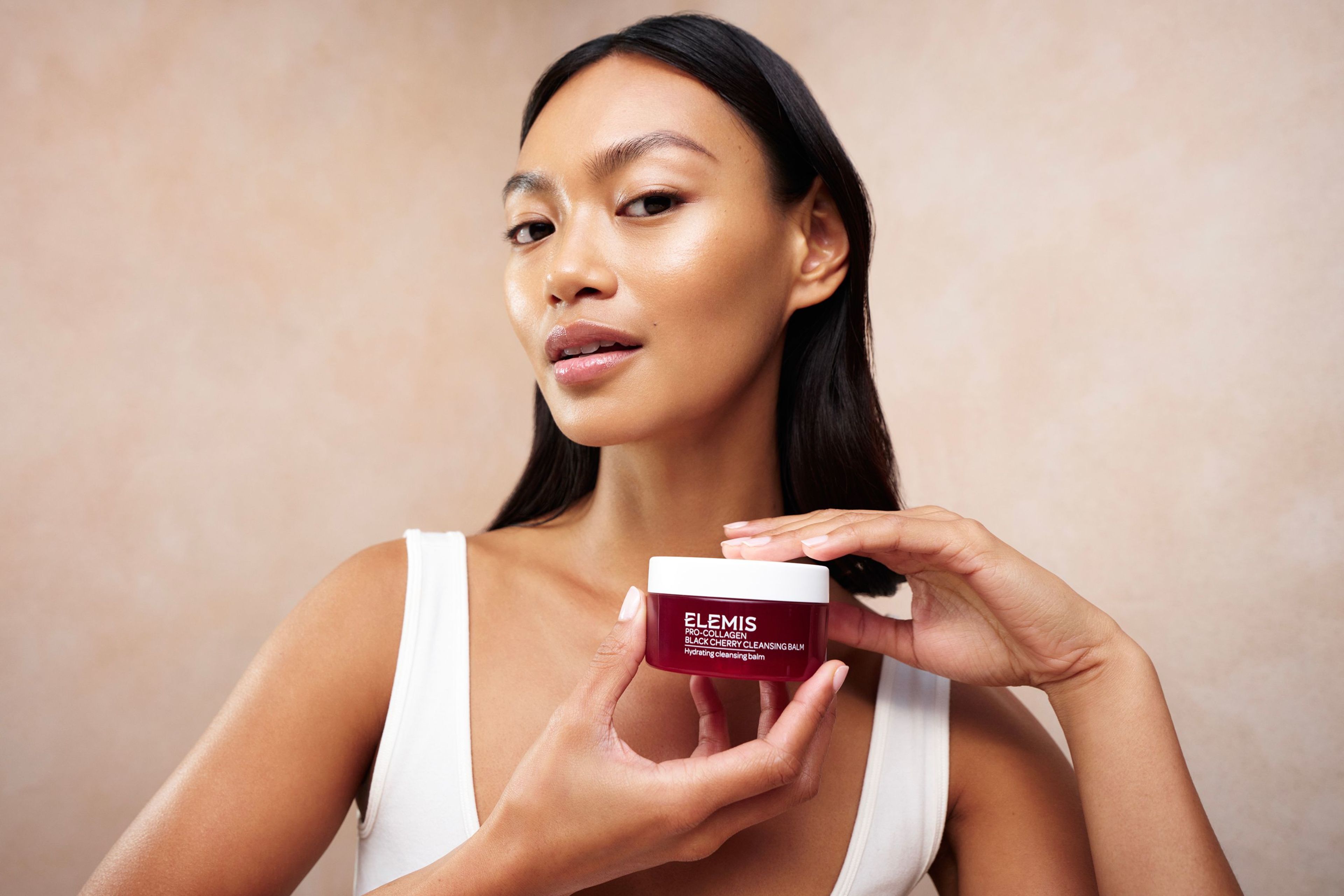 Nuovo vasetto di balsamo detergente Pro-Collagen Black Cherry Elemis circondato da ciliegie, mandorle e baccelli di vaniglia.