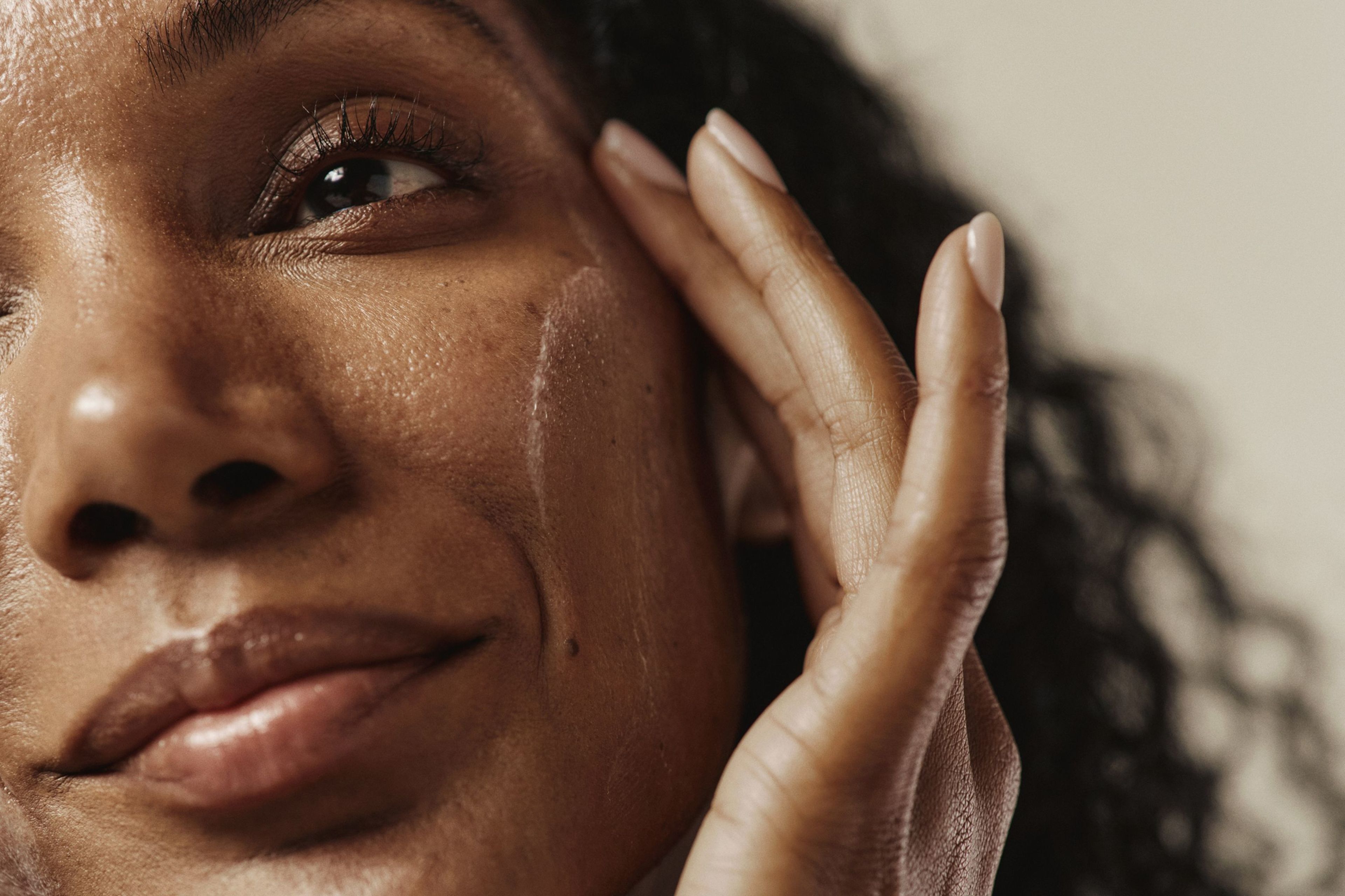 Close-up of a person with dark skin applying cream to their cheek.