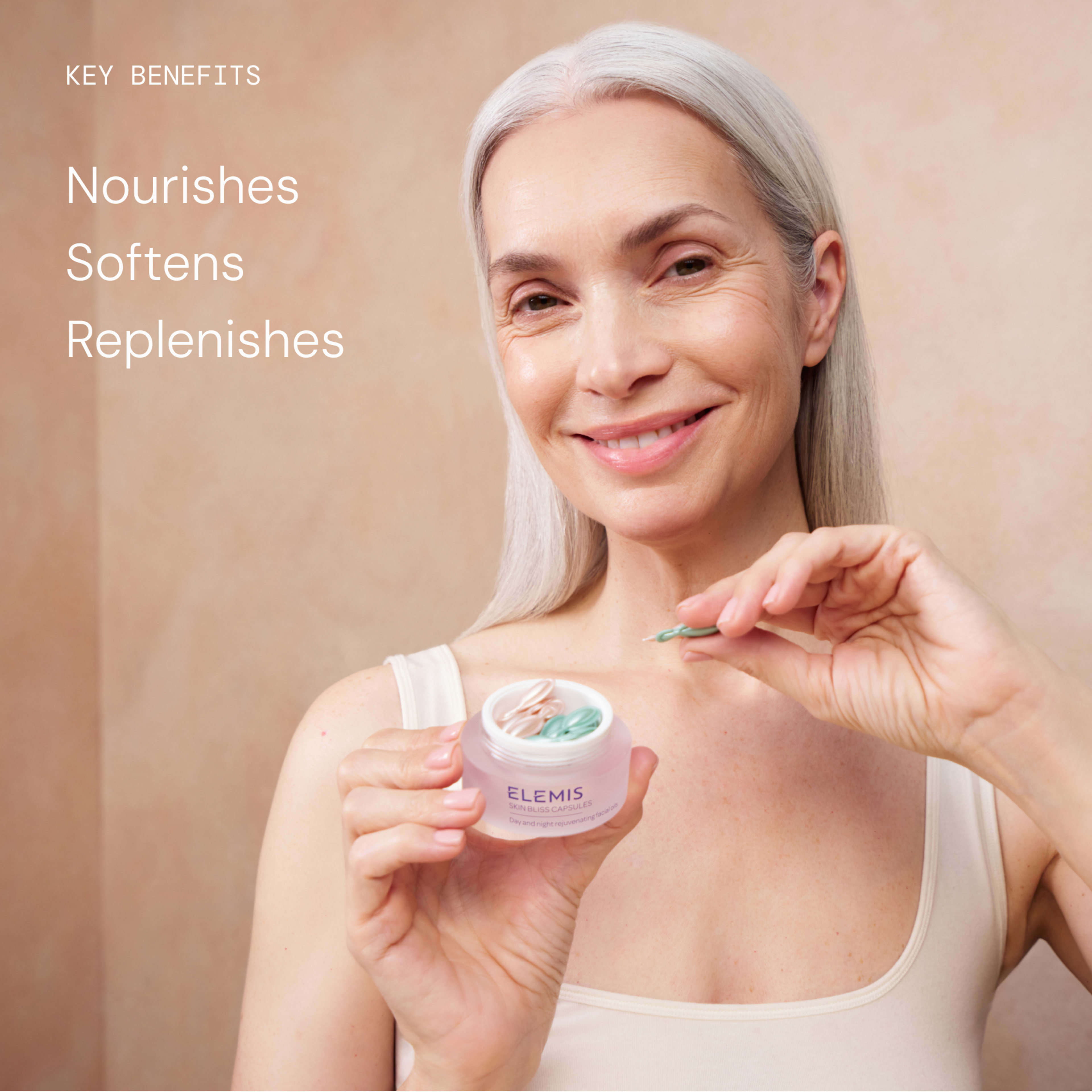 Smiling older woman in a vest holding an open ELEMIS skincare pot and applying a small amount with a spatula. On the left, text reads: “Key benefits: nourishes, softens, replenishes.”