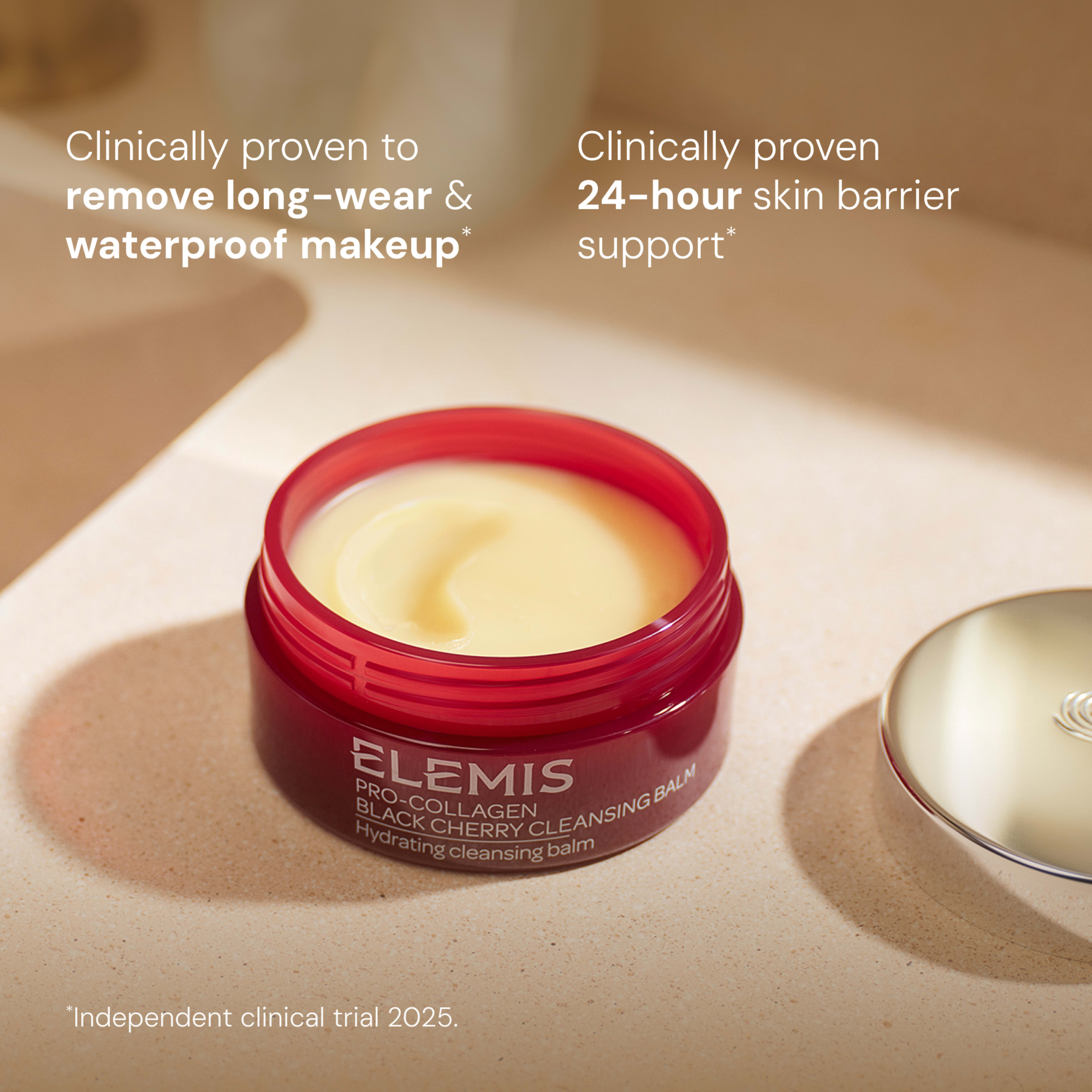 ELEMIS Pro-Collagen Black Cherry Cleansing Balm jar open on a bathroom surface, showing the pale yellow balm with the silver lid beside it. On-image text highlights that it is clinically proven to remove long-wear and waterproof makeup and provide 24-hour skin barrier support, with an independent clinical trial in 2025.