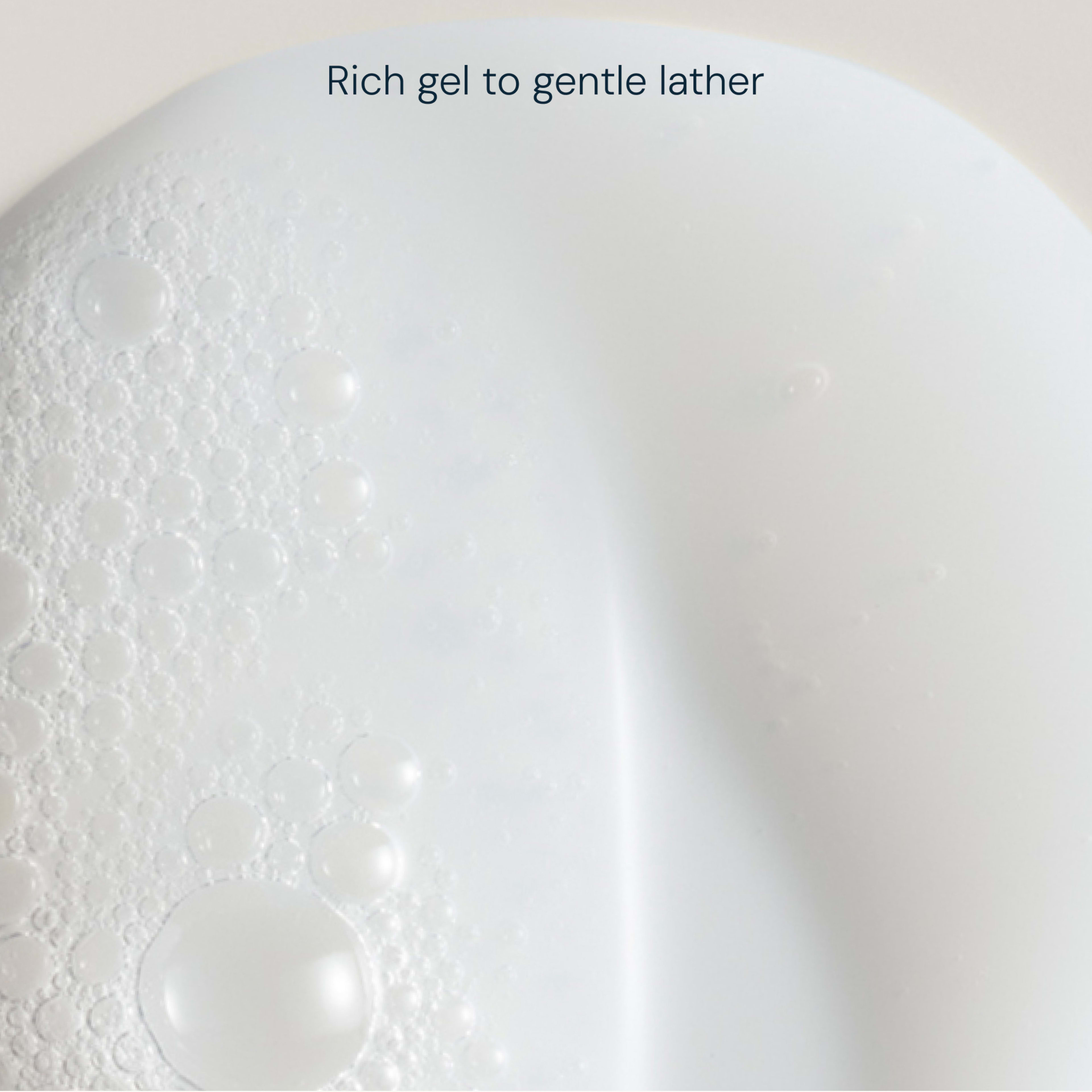 Close-up of white cleansing gel with bubbles and foam, showing its rich texture. Text reads: “Rich gel to gentle lather”.