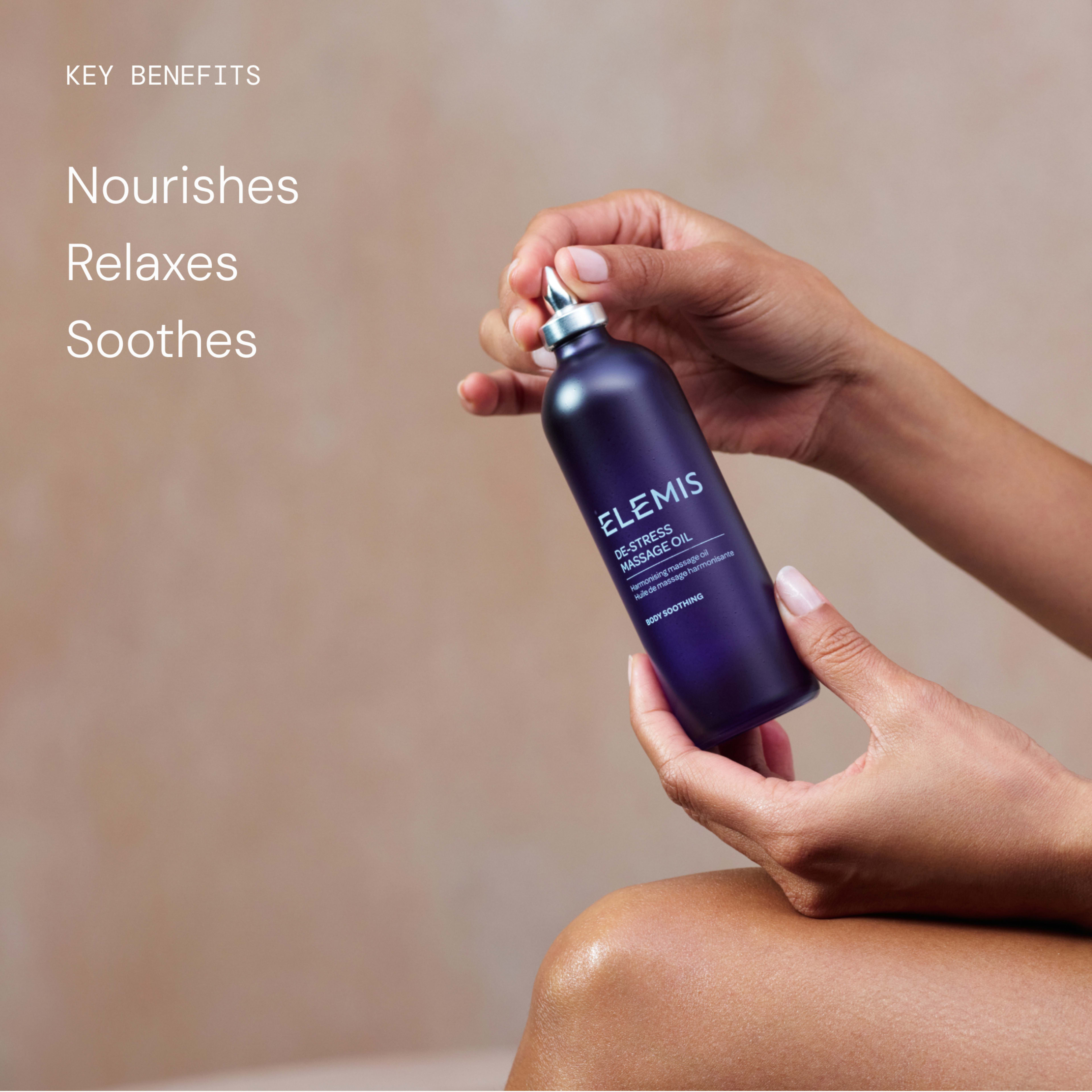Hands holding an ELEMIS De-Stress Massage Oil bottle against a neutral background, with on-image text reading: "Key benefits: nourishes, relaxes, soothes."
