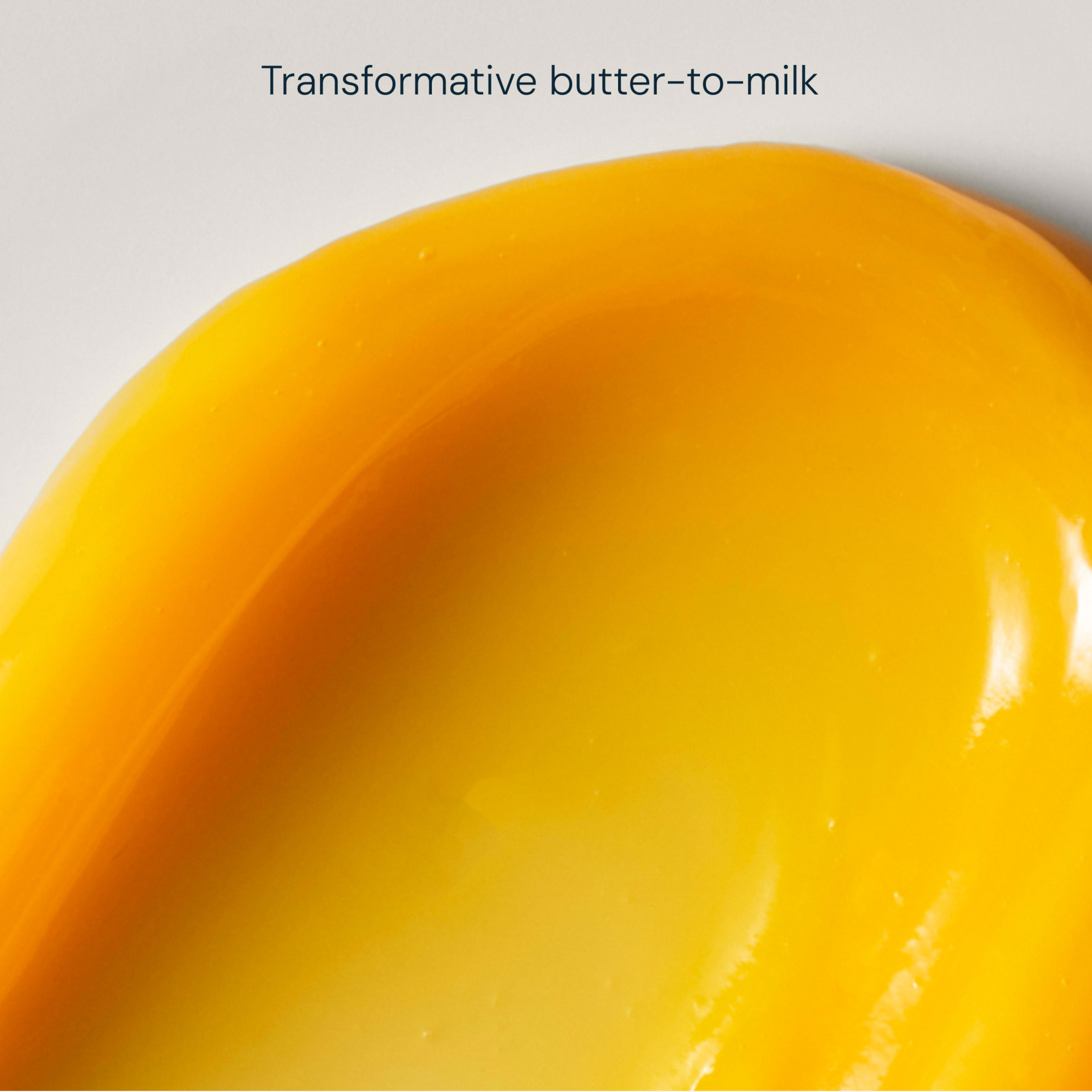 Close-up yellow cleansing balm swatch on a pale background, showing a glossy, melting texture with the caption "Transformative butter-to-milk".