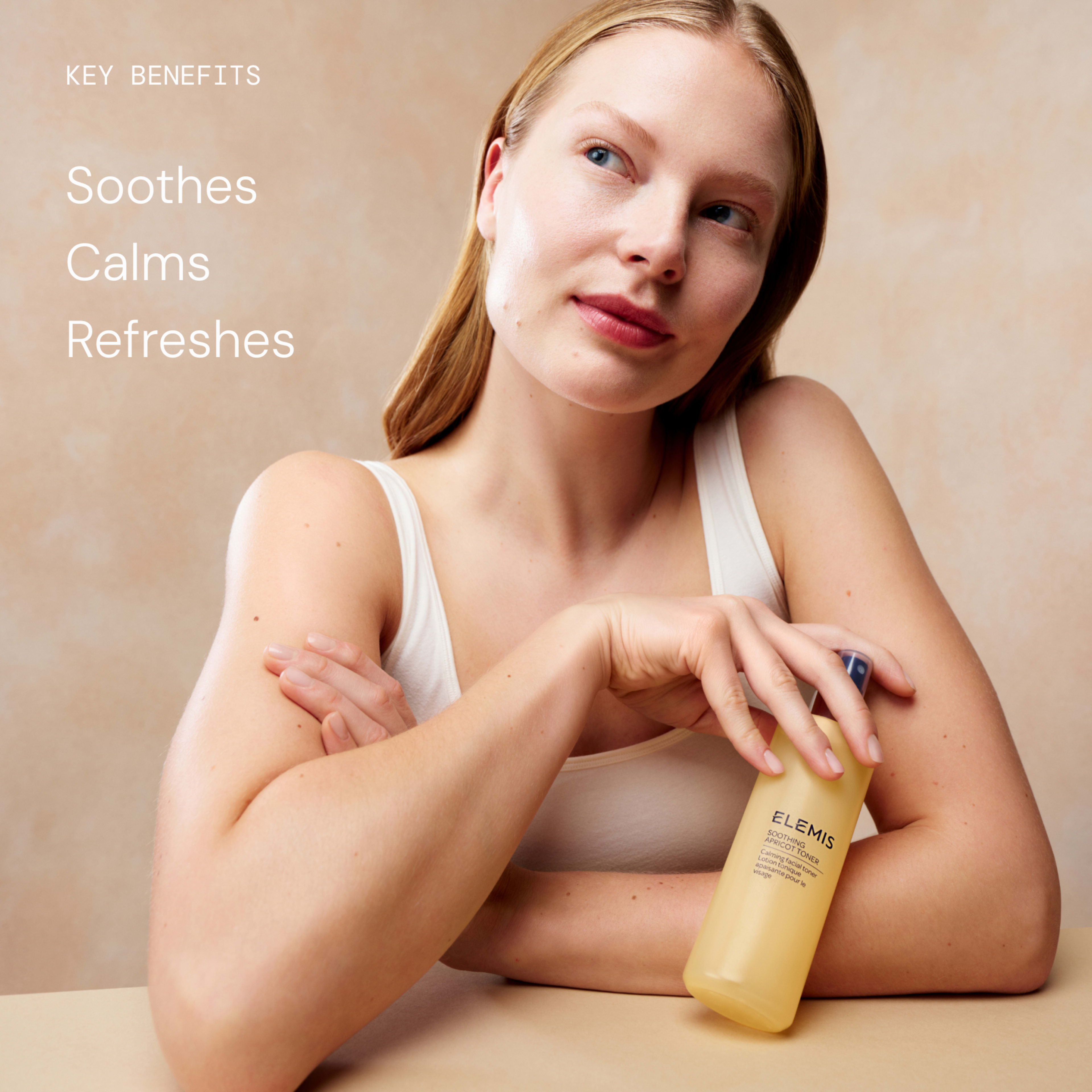 Woman in a white vest resting her arms on a table, holding a yellow ELEMIS bottle and looking thoughtfully to the side, against a neutral background. On the left, text reads: “Key benefits – Soothes, Calms, Refreshes”.