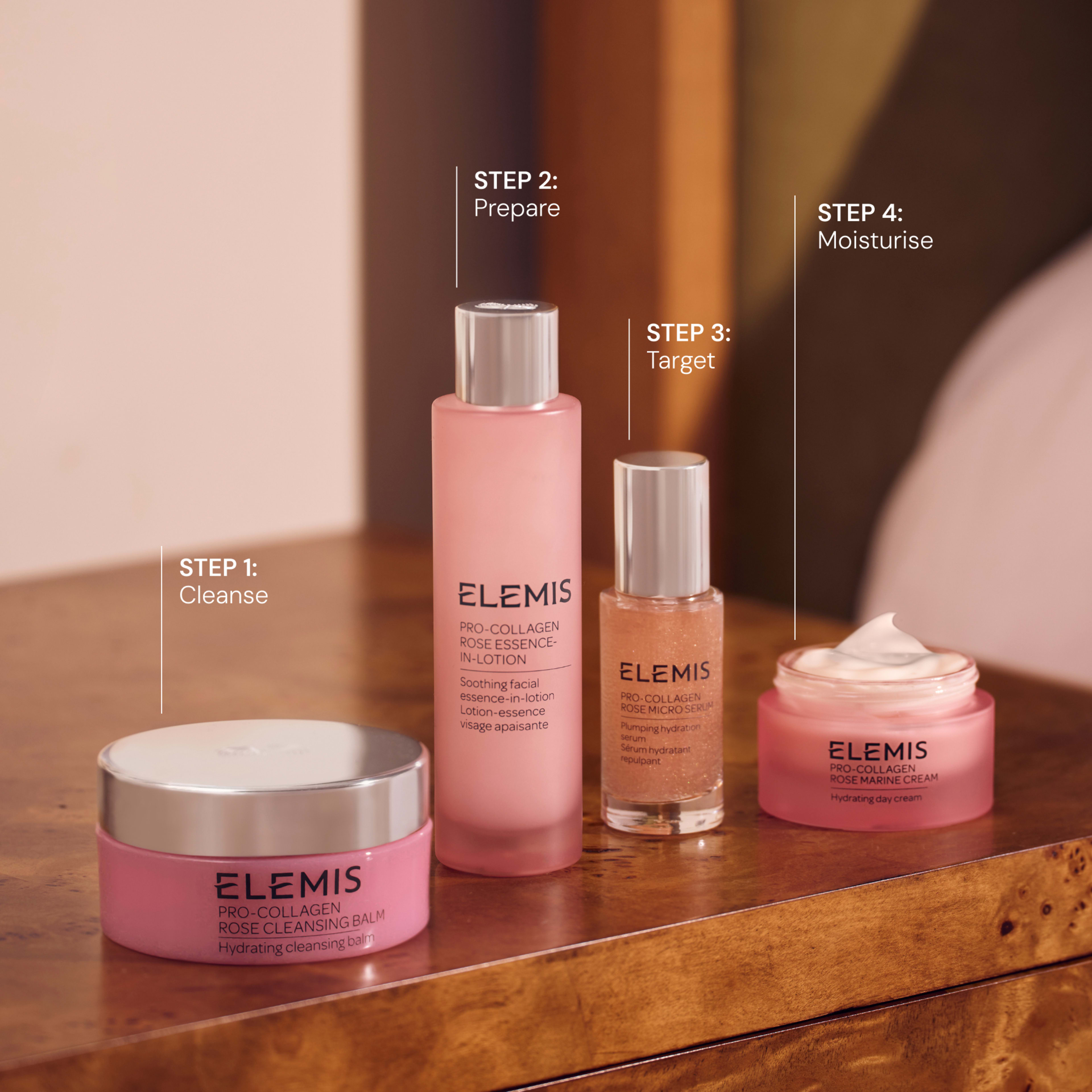 Four pink ELEMIS Pro-Collagen Rose skincare products on a wooden table, labelled as a four-step routine: step 1 cleanse, step 2 prepare, step 3 target and step 4 moisturise, showing cleansing balm, essence-in-lotion, micro serum and marine cream.