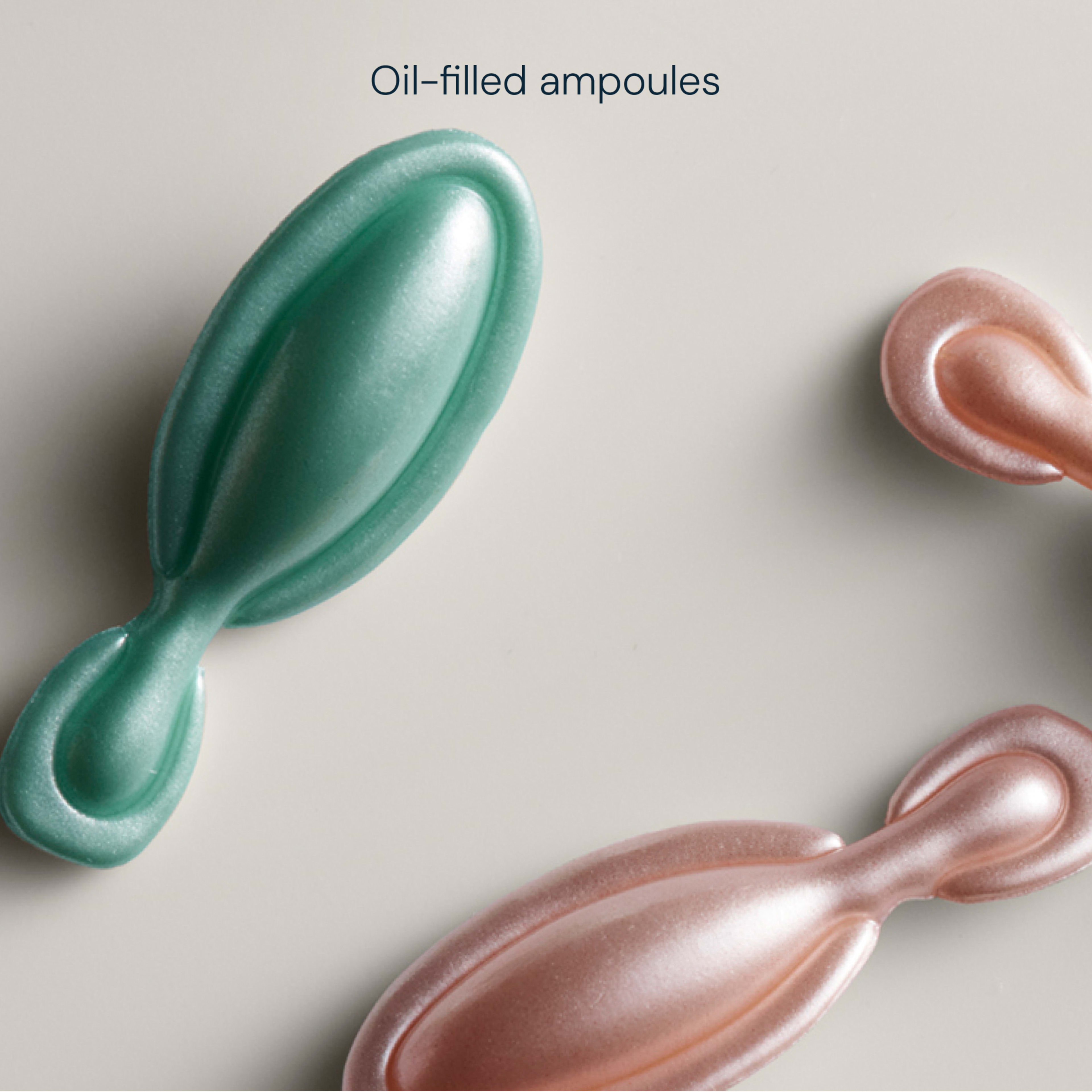 Close-up of pastel green and pink oil-filled skincare ampoules on a pale background, with the words “Oil-filled ampoules” above.