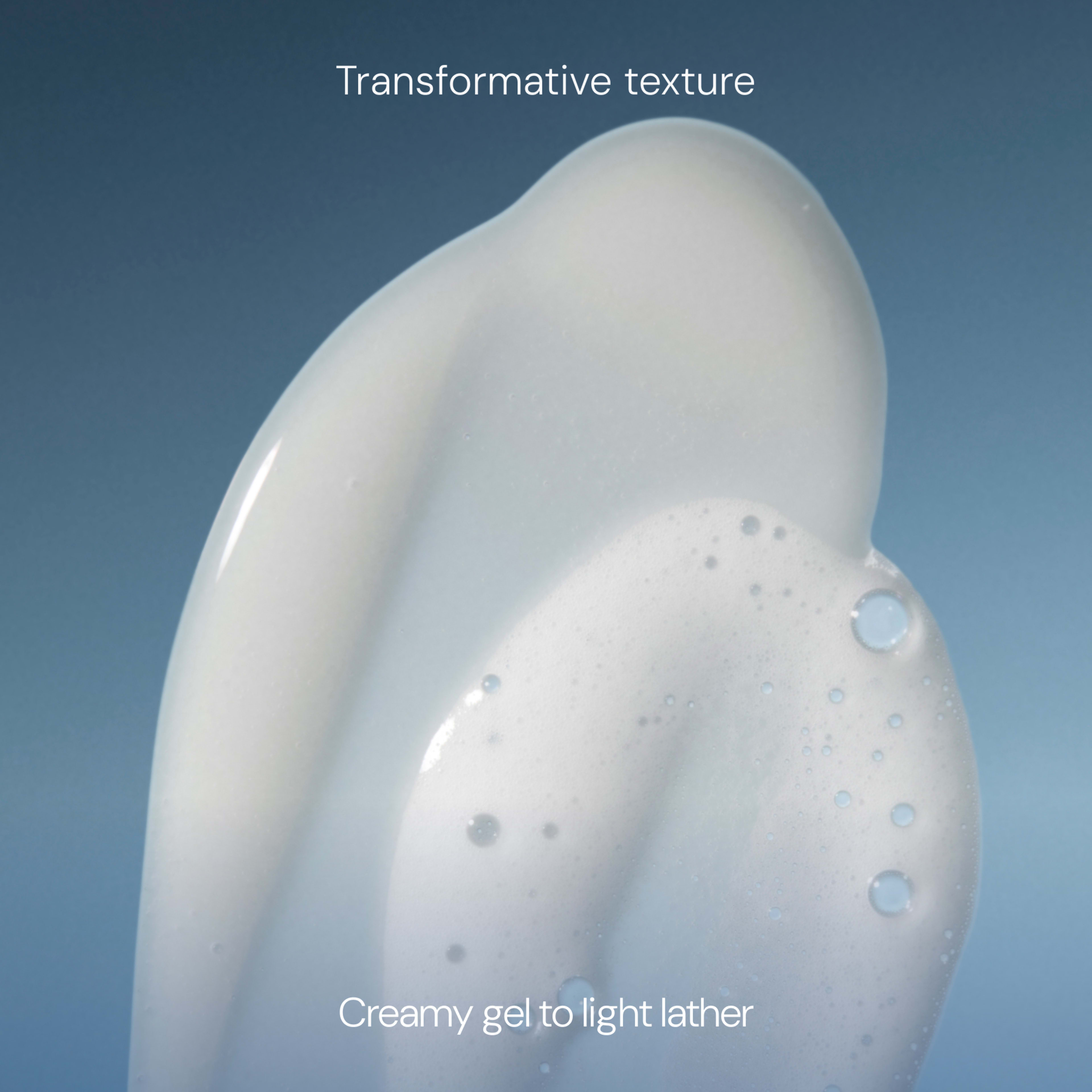Close-up of a pale, foamy cleanser against a blue background with bubbles showing its texture, overlaid with the text "Transformative texture" and "Creamy gel to light lather".