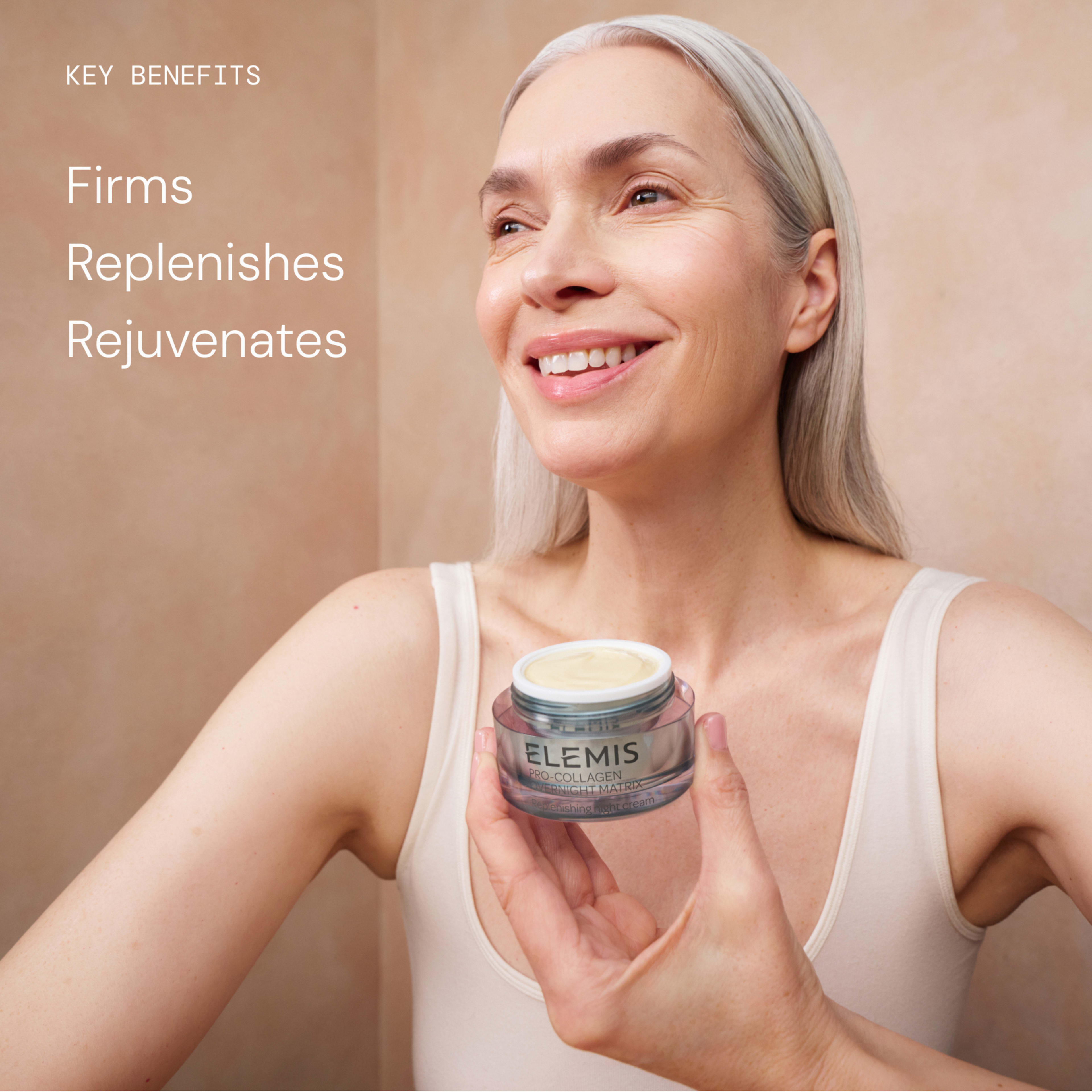 Smiling older woman with long grey hair in a vest holds an open ELEMIS Pro-Collagen cream jar towards the camera. On the left, text reads: "Key benefits: Firms, Replenishes, Rejuvenates."