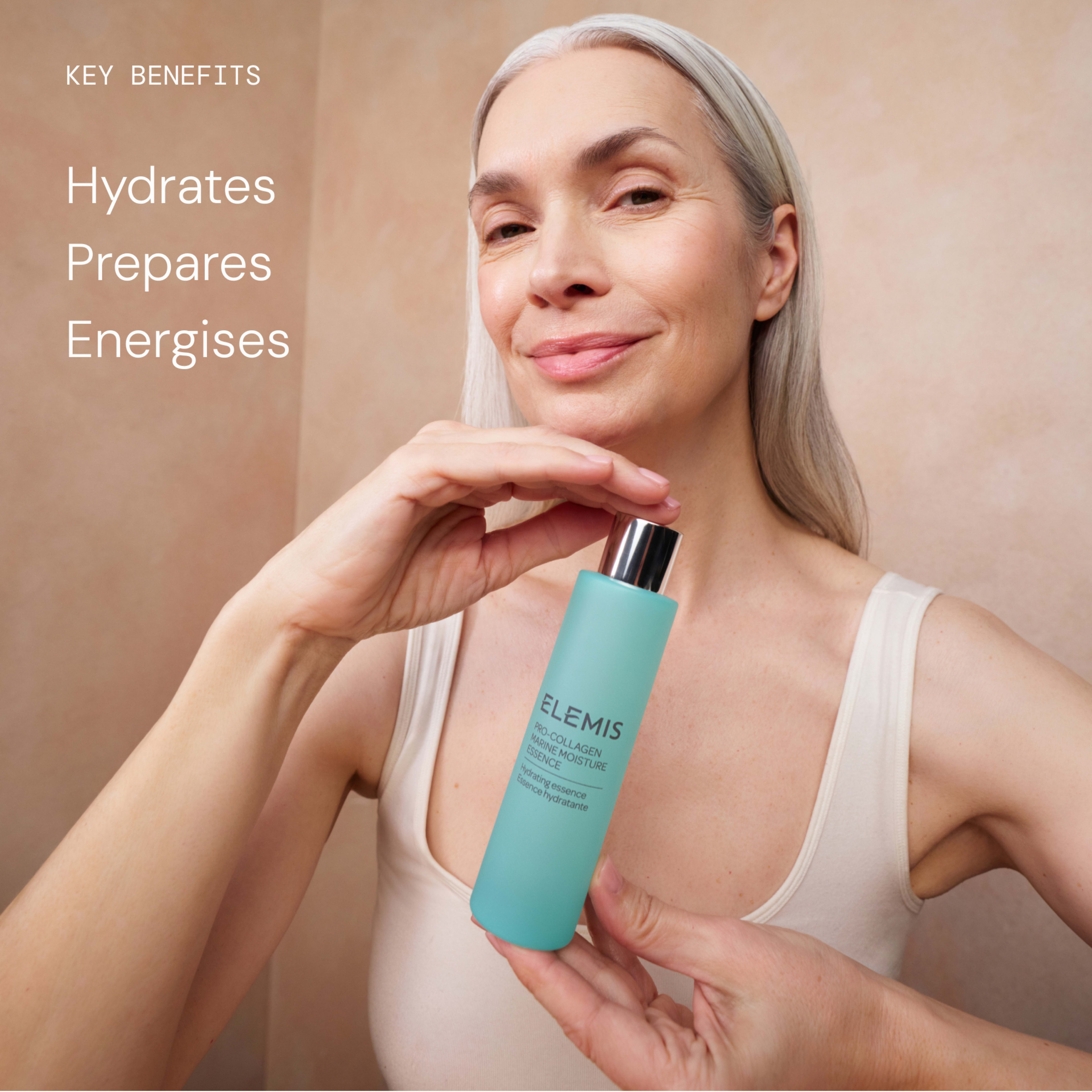 Smiling woman with long grey hair holds a turquoise ELEMIS facial skincare bottle towards the camera. Text on the left reads: "Key benefits: Hydrates, Prepares, Energises."