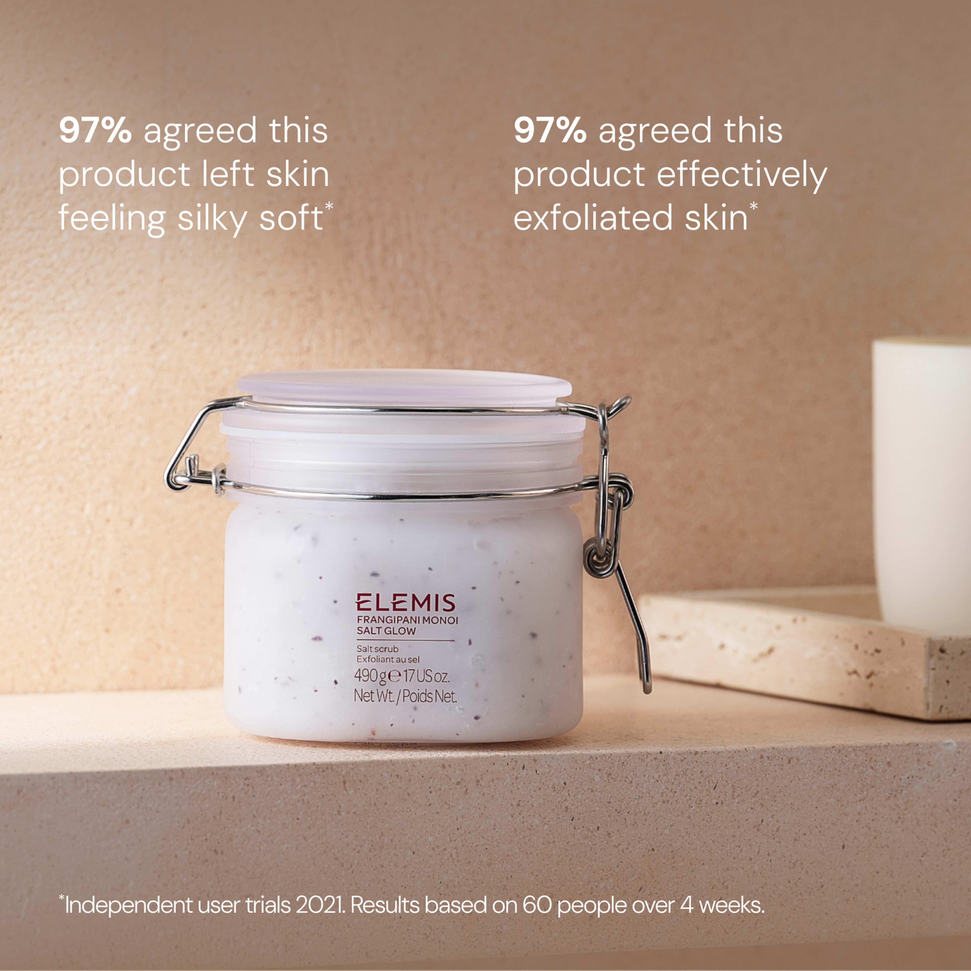 ELEMIS Frangipani Monoi Salt Glow exfoliating scrub in a glass jar on a neutral bathroom surface, with a lit candle in the background. On-image text: “97% agreed this product left skin feeling silky soft”, “97% agreed this product effectively exfoliated skin”.