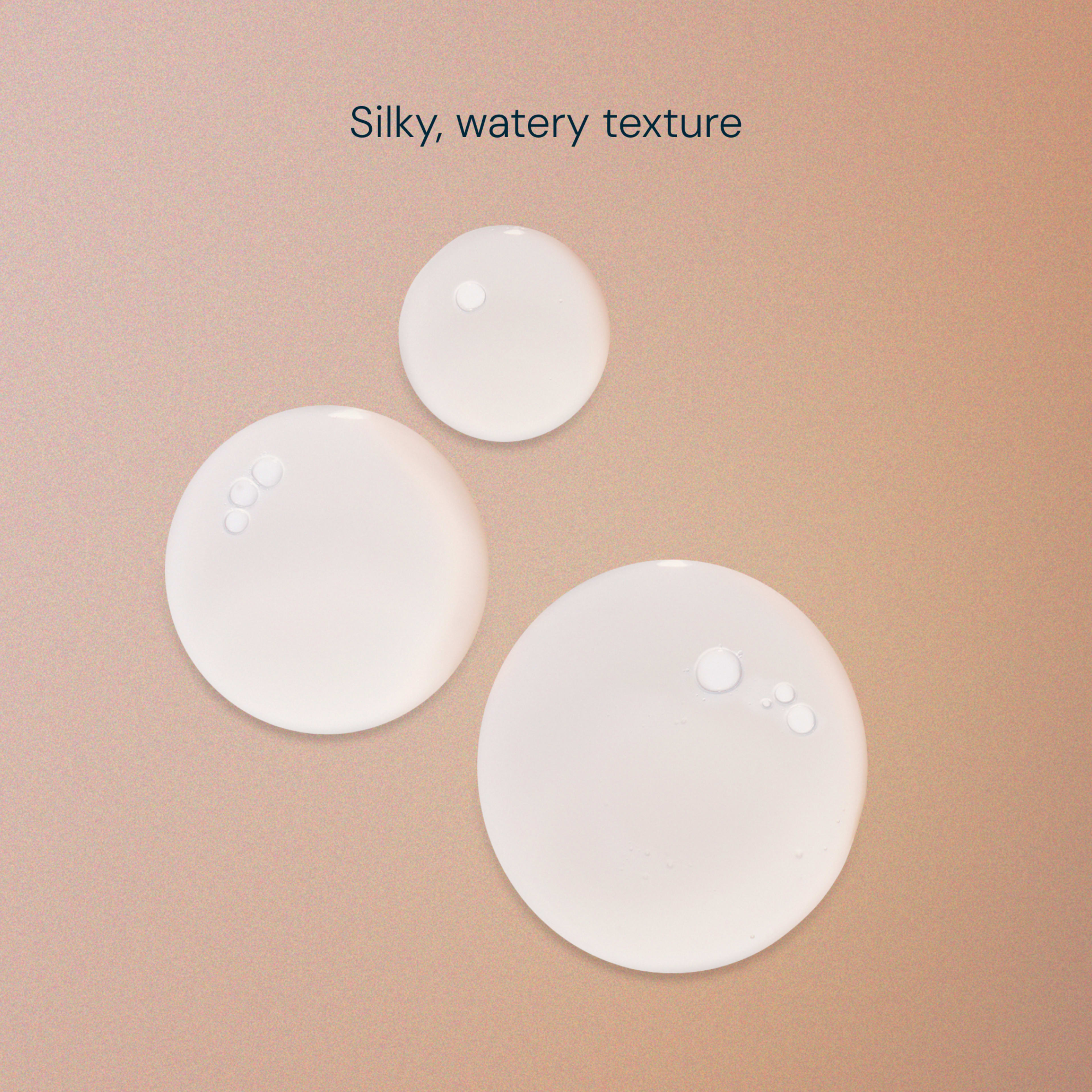 Clear serum droplets on a soft peach background, illustrating a fluid skincare formula with a silky, watery texture.