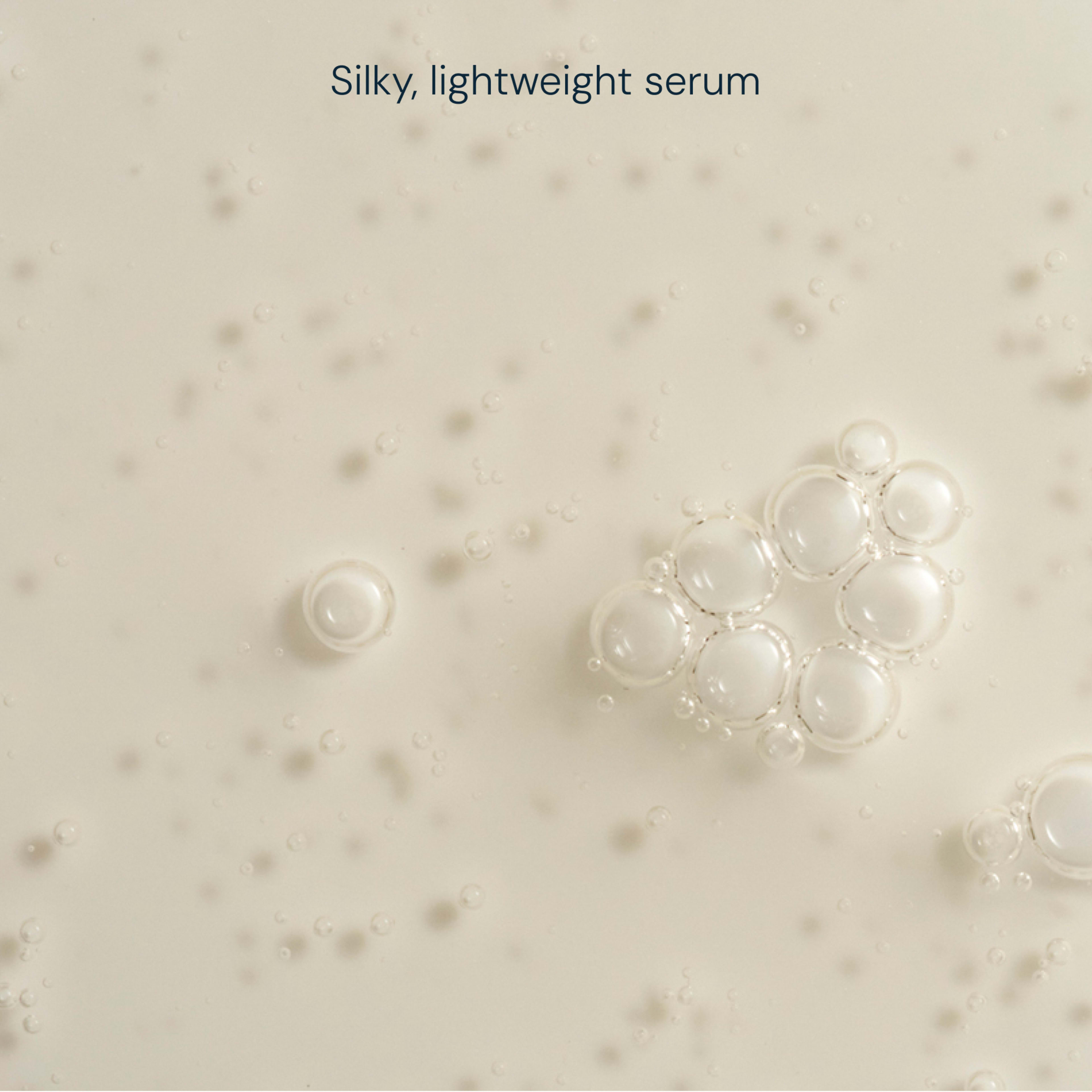 Close-up of a pale, silky, lightweight serum texture dotted with small bubbles, with the text “Silky, lightweight serum” at the top.