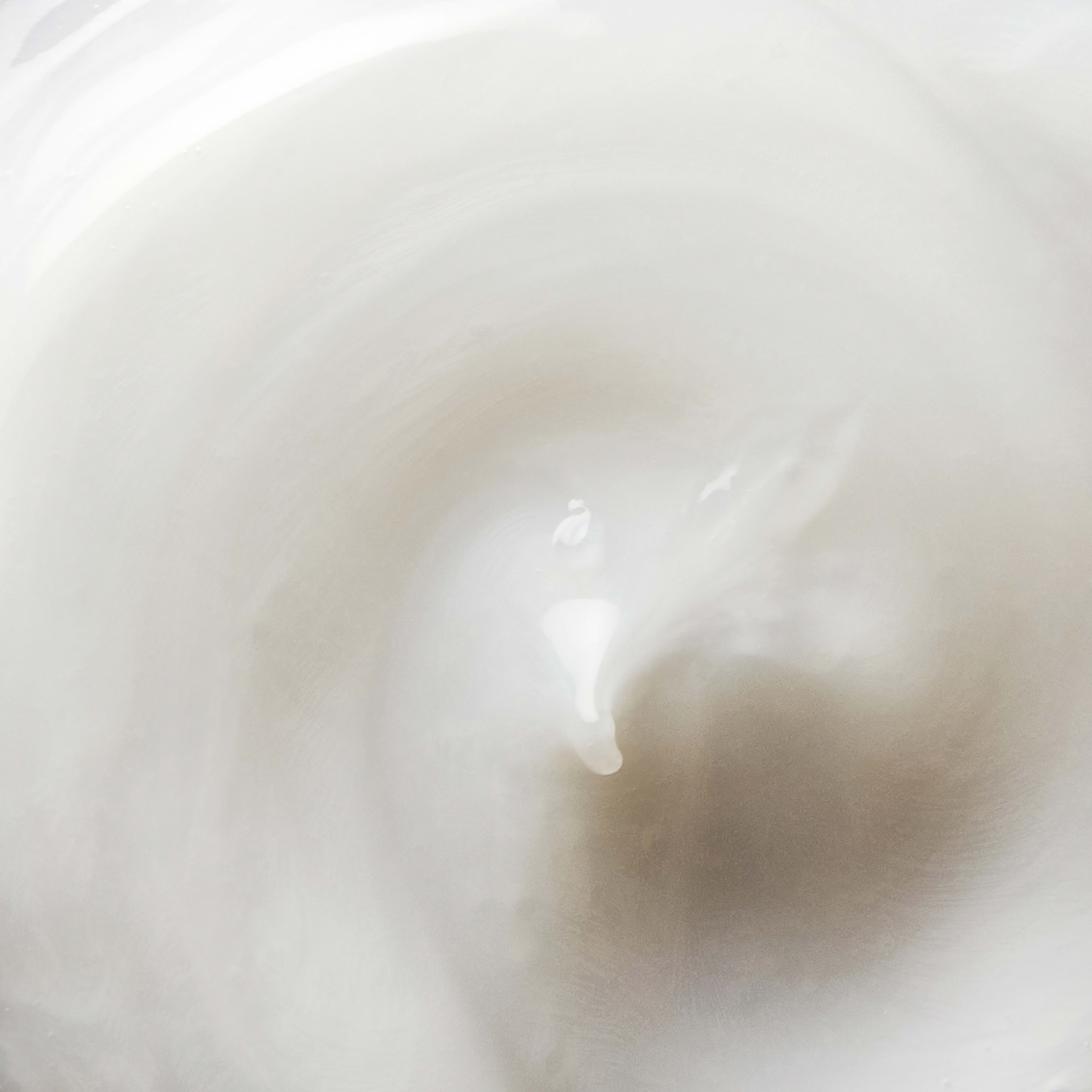 Close-up swatch of glossy white cream forming soft swirling peaks and curves.