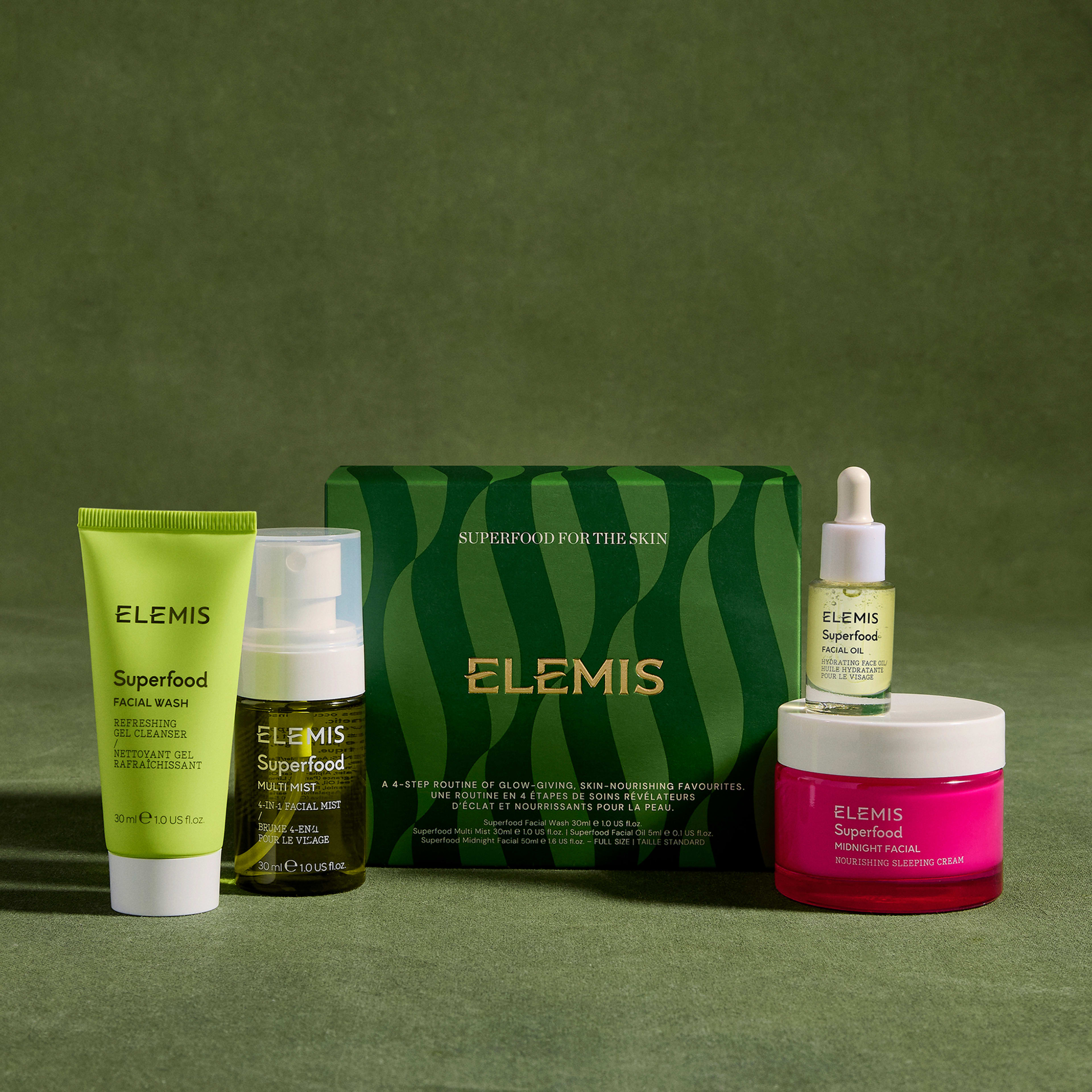 ELEMIS Superfood skincare gift set arranged on a green background, featuring Facial Wash, Multi Mist, facial oil, Overnight Facial moisturiser and a central green striped box labelled “SUPERFOOD FOR THE SKIN”.