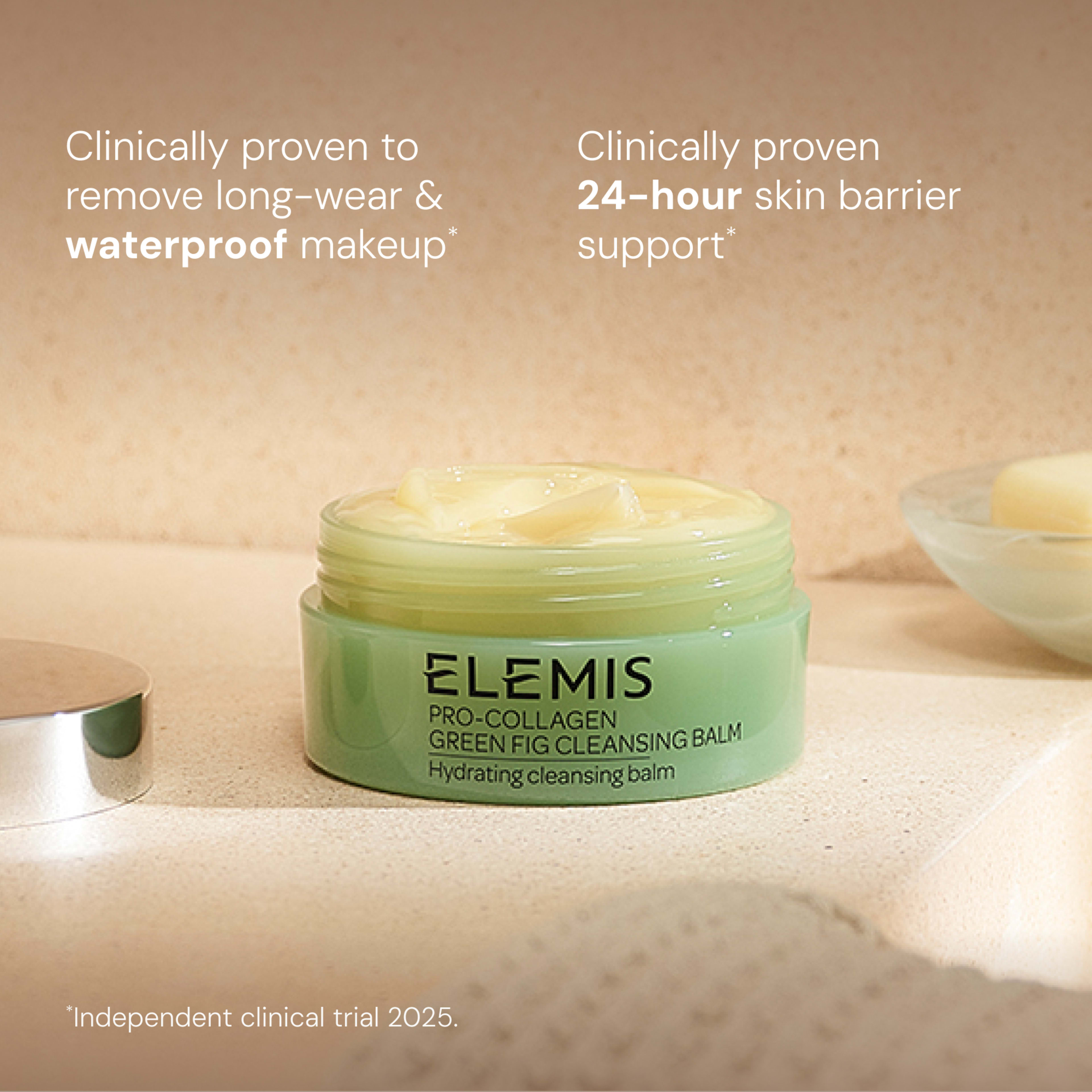 ELEMIS Pro-Collagen Green Fig Cleansing Balm jar on a bathroom counter with creamy balm visible. On-image text states it is clinically proven to remove long-wear and waterproof makeup and provide 24-hour skin barrier support, with an independent clinical trial in 2025.
