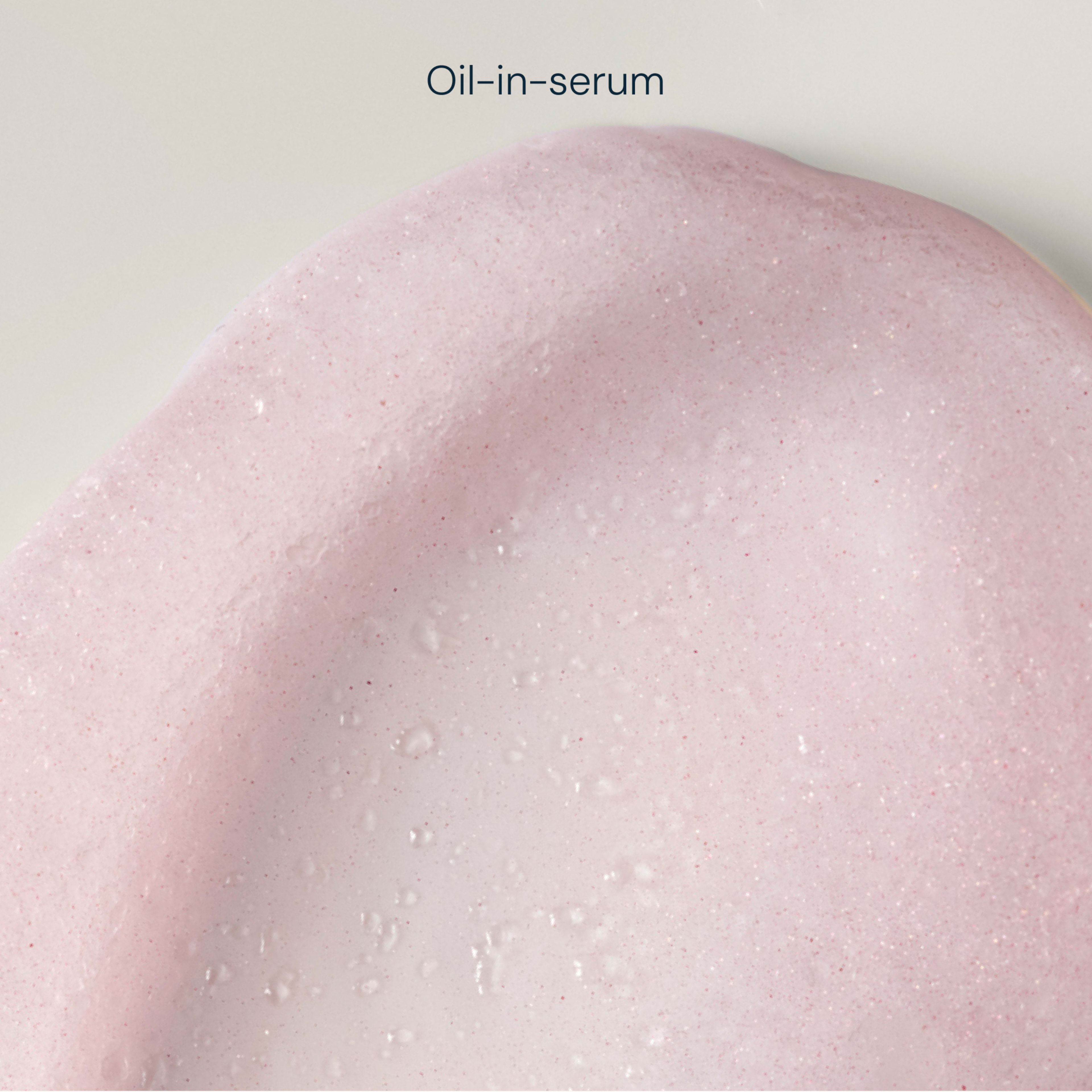 Close-up swatch of a pale pink, foamy oil-in-serum texture with tiny bubbles and a creamy, fluid finish.