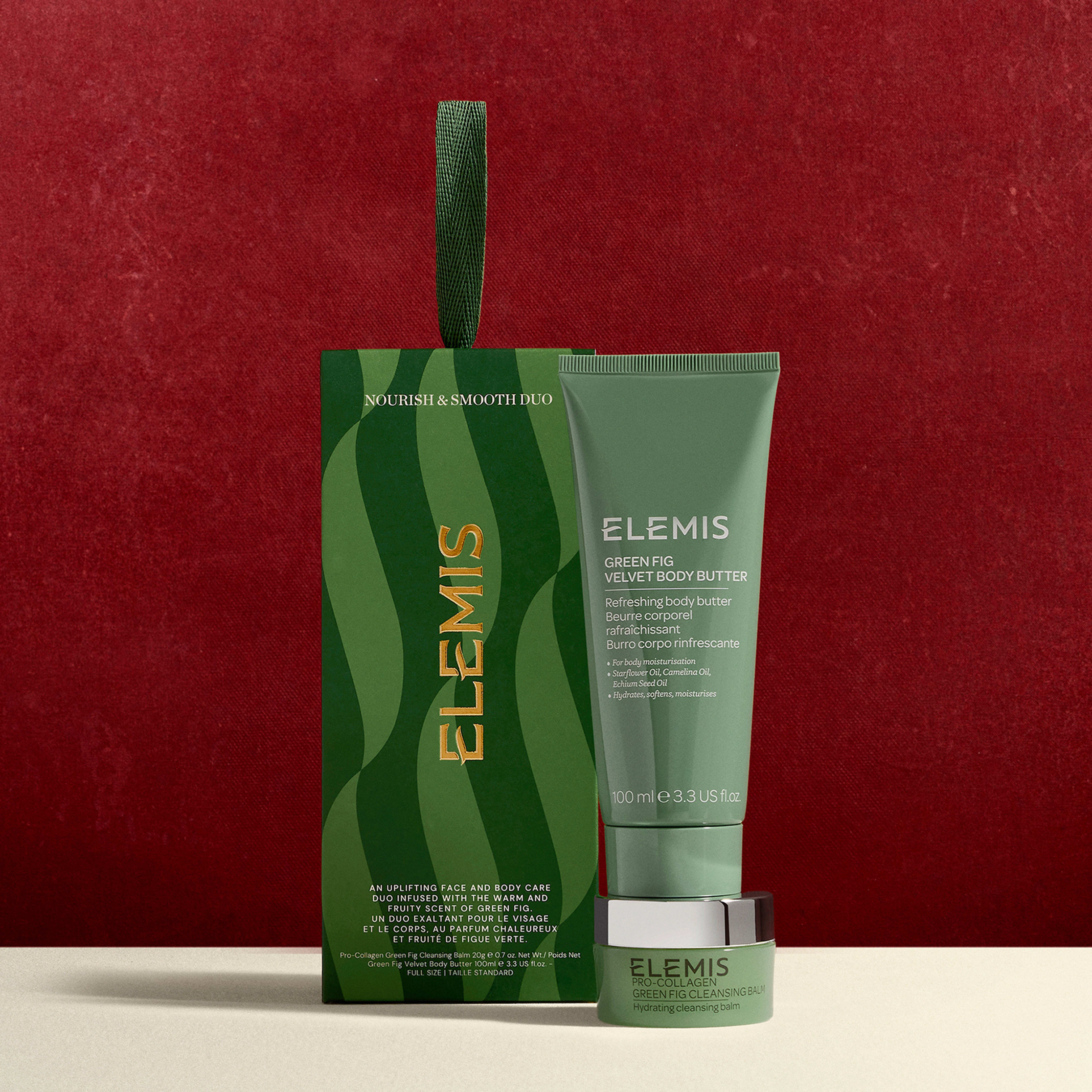 ELEMIS Nourish & Smooth Duo gift set against a red backdrop, including Green Fig Velvety Body Butter 100ml and a small matching jar, in green packaging with wavy pattern and hanging ribbon.